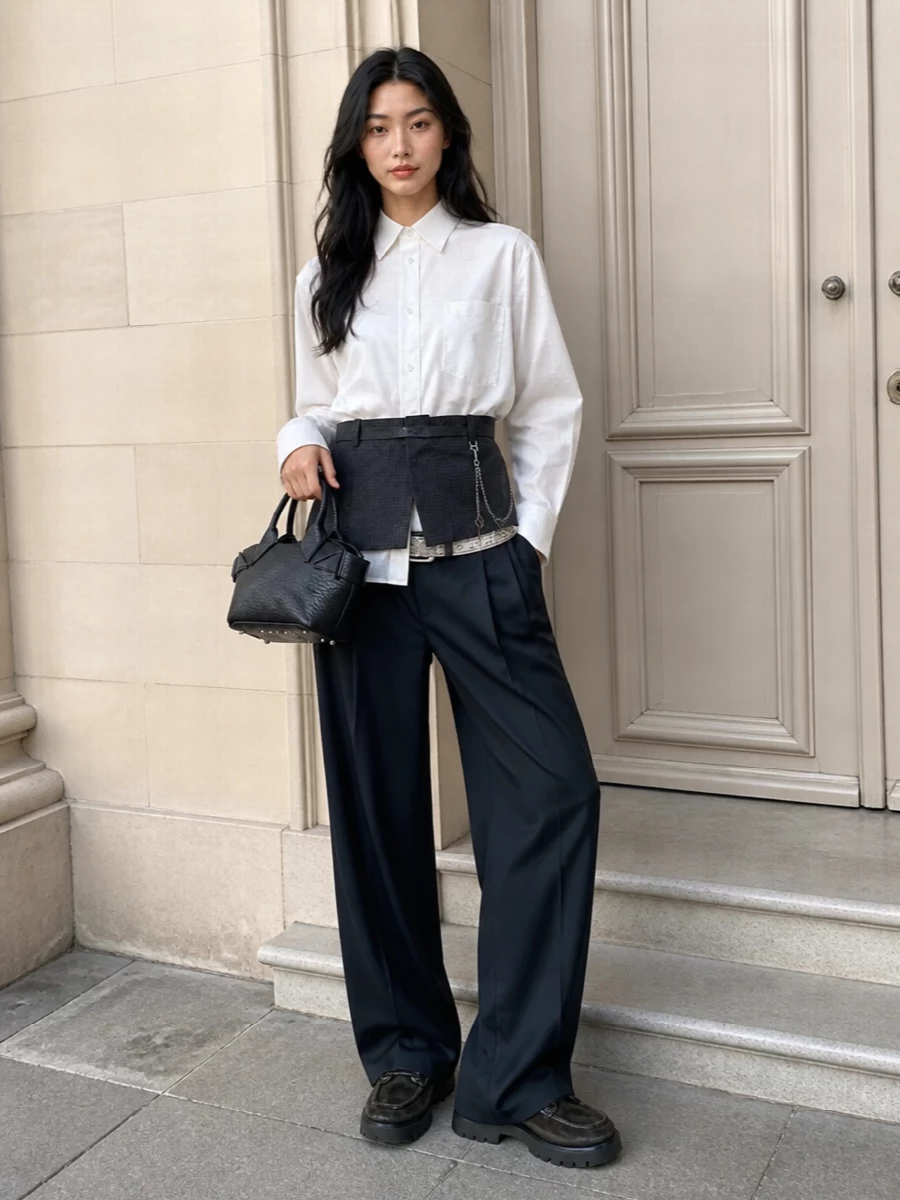 Alexander Wang’s engineered shirt sits over tailored wide-leg trousers for a long, graphic line in soft white and charcoal. Chunky lace-ups and a structured mini tote keep the mood sharp and urban, while a slim studded belt quietly picks up the shirt’s metal hardware. It is office-appropriate with an intentional downtown slant you do not have to over-style.