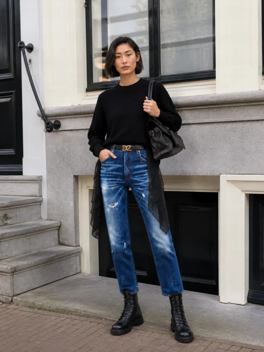 Core Dsquared2 attitude, this pairing leans into distressed high-waist denim with a black chiffon-tail sweatshirt for a streetwear take that still feels considered. Chunky combat boots and a structured black satchel keep the palette tight and urban, while the logo belt quietly defines the waist so the straight leg hangs cleanly over the hardware-heavy boots. It is a confident city uniform that shifts from daytime errands to low-key drinks without needing a change.