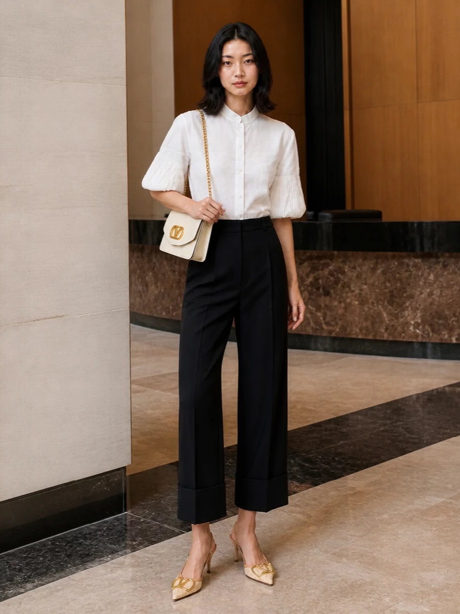 A crisp white sculpted shirt meets cropped black tailoring for a romantic yet incisive take on modern polish. Natural raffia-textured slingbacks and a buttercream chain bag soften the contrast, keeping the palette luminous while the silhouette stays sharp from daylight meetings to late gallery dinners.
