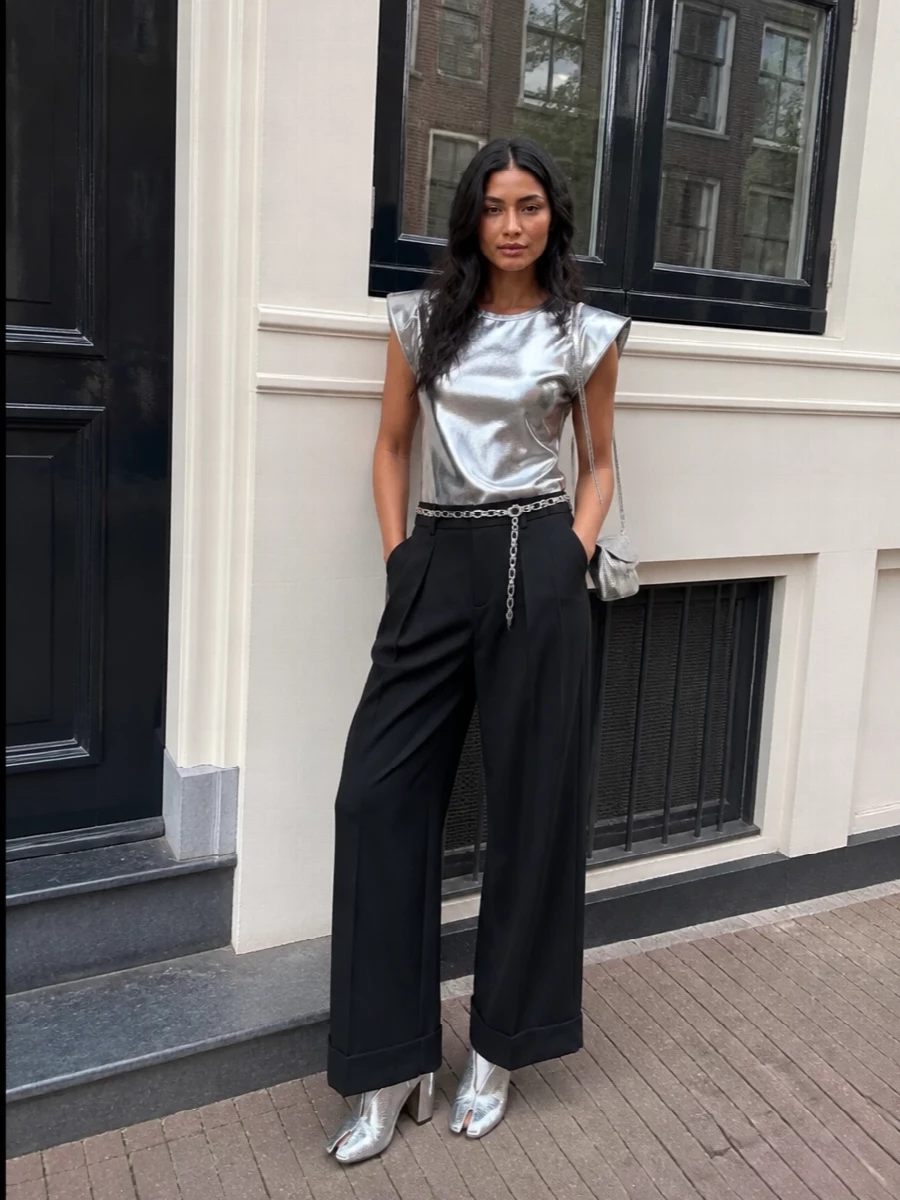 Junya’s metallic top sits over strong black wide-leg tailoring, so the shine reads deliberate and architectural rather than costume. Hard, reflective surfaces stay focused at the torso, feet, and bag, with a chain belt tracing a clean vertical from shoulder to cuffed hem. The result is a futurist, night-out uniform that still feels rigorously composed and city-ready.