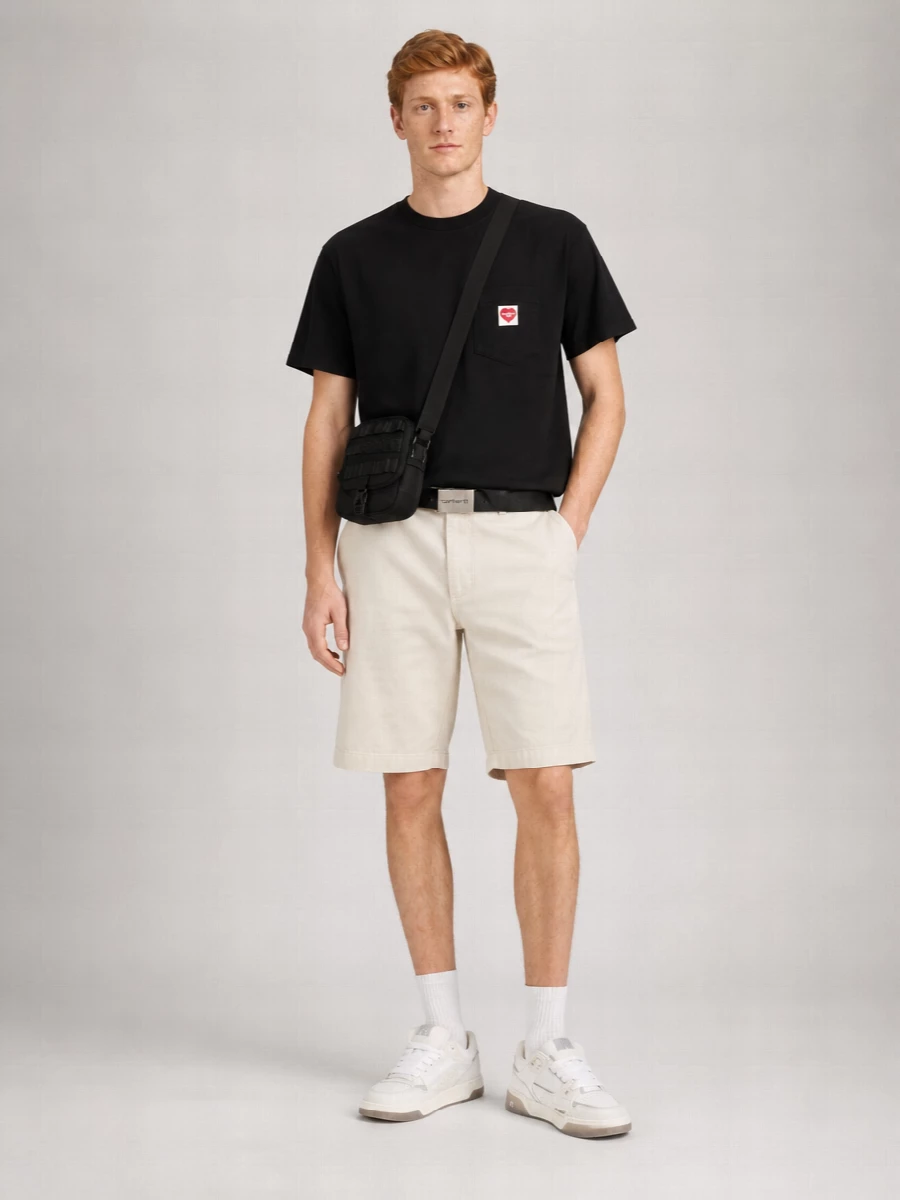 A black Carhartt tee sits against light beige cargo shorts for a clean, skate-leaning mix of contrast and utility. Off white gum-sole sneakers keep everything relaxed and grounded, while a compact black crossbody and matching webbing belt add just enough street hardware without disturbing the minimalist mood.