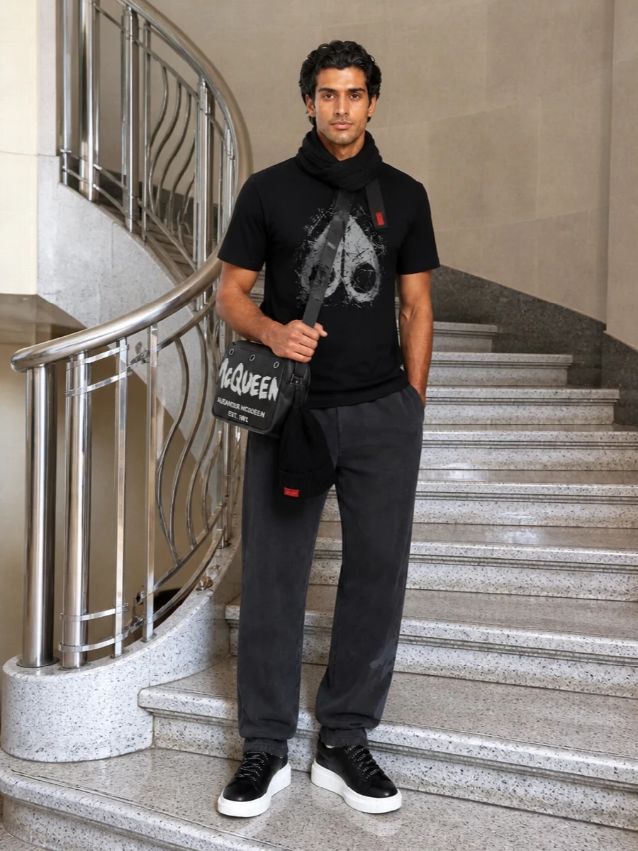 A dark, graphic street set built around the Moose Knuckles tee, this pairing leans into washed charcoals and deep black for a tight, monochrome story. The Off-White joggers and McQueen sneakers keep the lines clean but relaxed, while the McQueen crossbody and knit accessories push it firmly into designer off-duty territory with real city mileage.