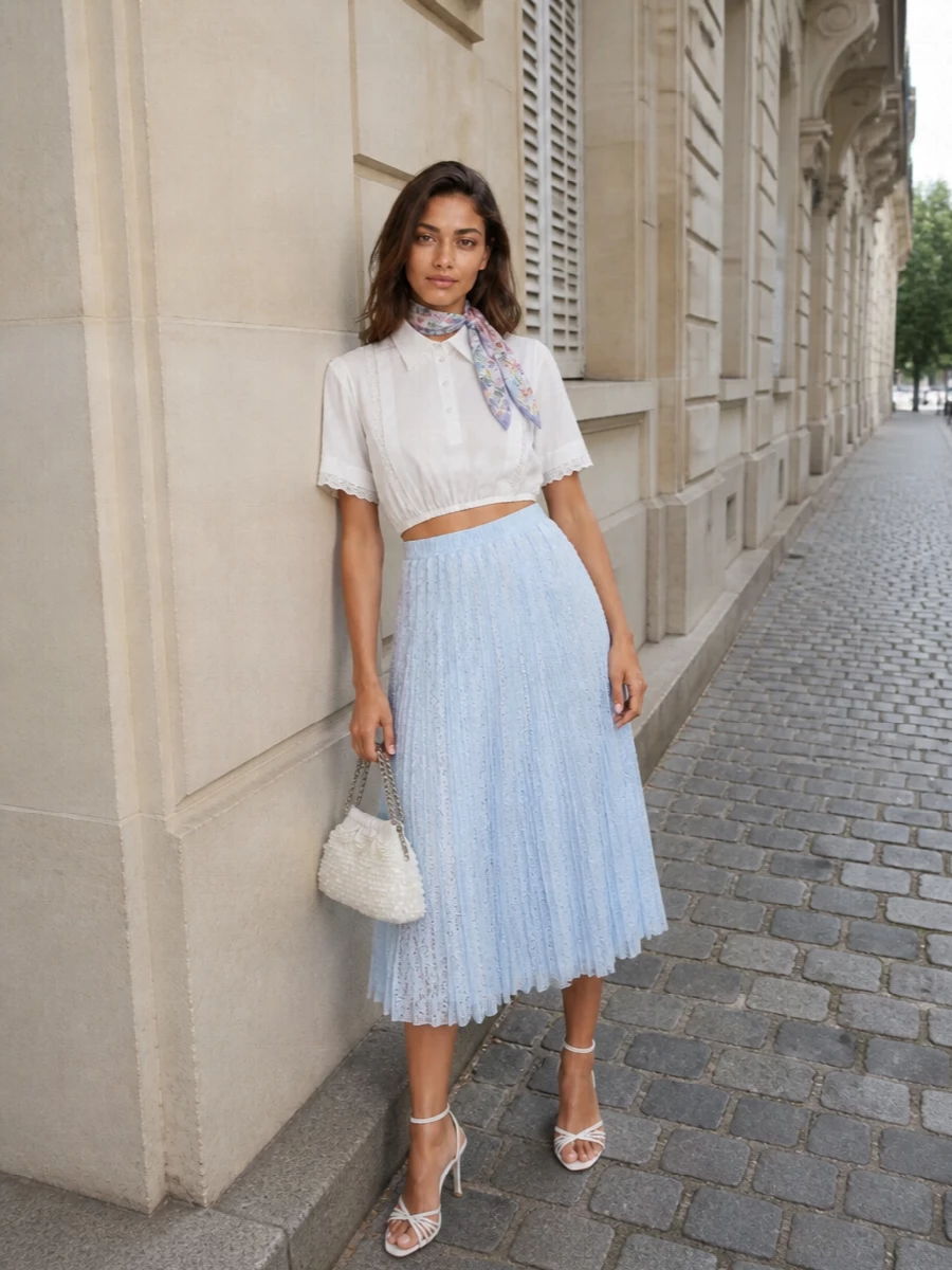 A frosted palette of light blue and soft white keeps this lace-on-lace pairing airy and romantic, with the cropped blouse meeting the elasticated waist to define the figure gently. Strappy white heels and a pearlescent clutch bring just enough shine for garden parties and summer cocktails while staying quietly polished. A floral silk scarf adds a whisper of colour that feels considered rather than decorative.