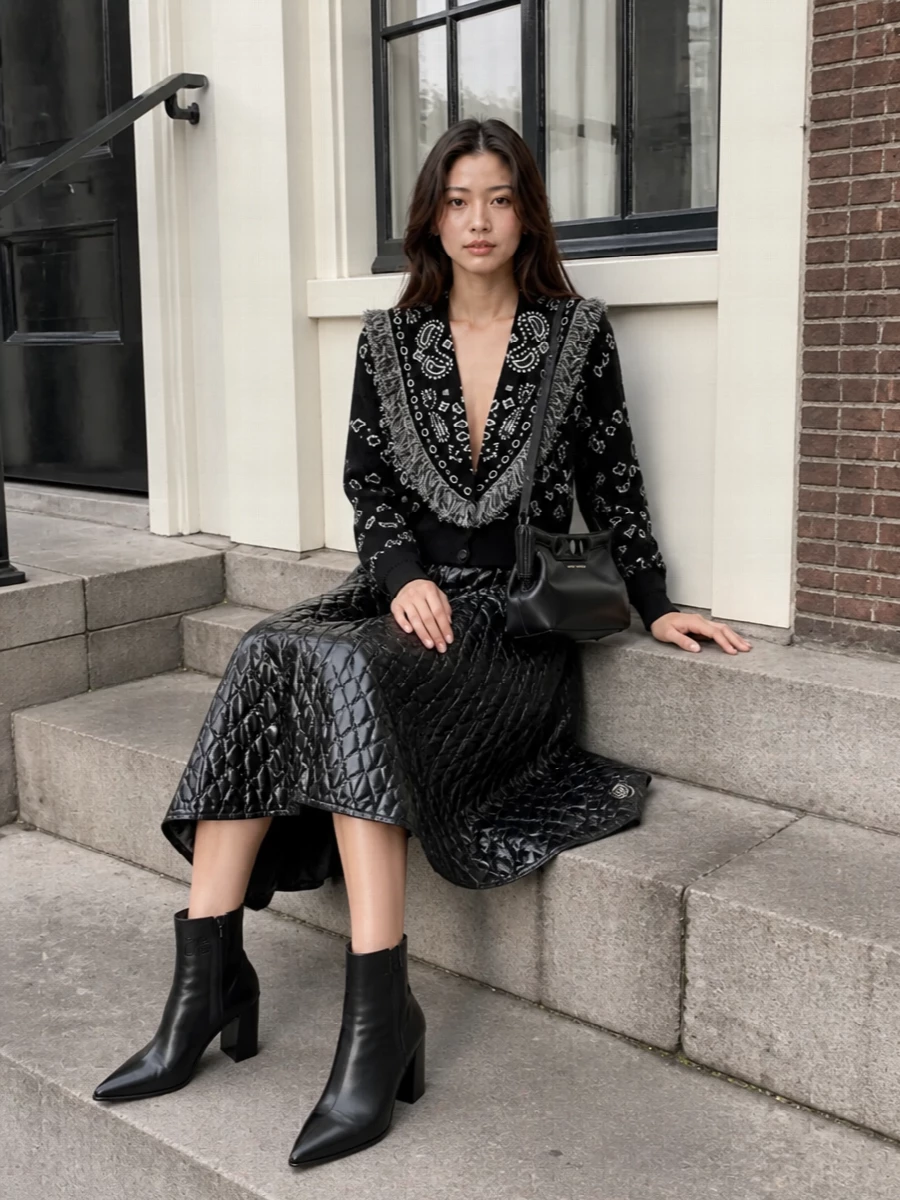 A bandana-fringed cropped cardigan tops a glossy quilted midi, turning winter textures into a graphic black-on-black statement. Sleek pointed ankle boots keep the volume disciplined and sharp, while a sculpted black crossbody adds that final hit of attitude. It is street-leaning but unmistakably polished, ready for city days that run late.