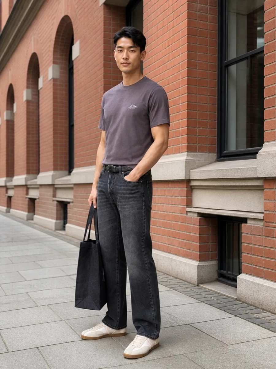 A washed charcoal-mauve tee sits over straight charcoal denim for a tight, low-contrast base that feels calm and considered. Off-white gum-sole trainers brighten the mix just enough, while a dark canvas tote and slim distressed belt keep everything grounded and city-ready. The result is relaxed streetwear with a quietly polished edge that works from coffee runs to long days in town.