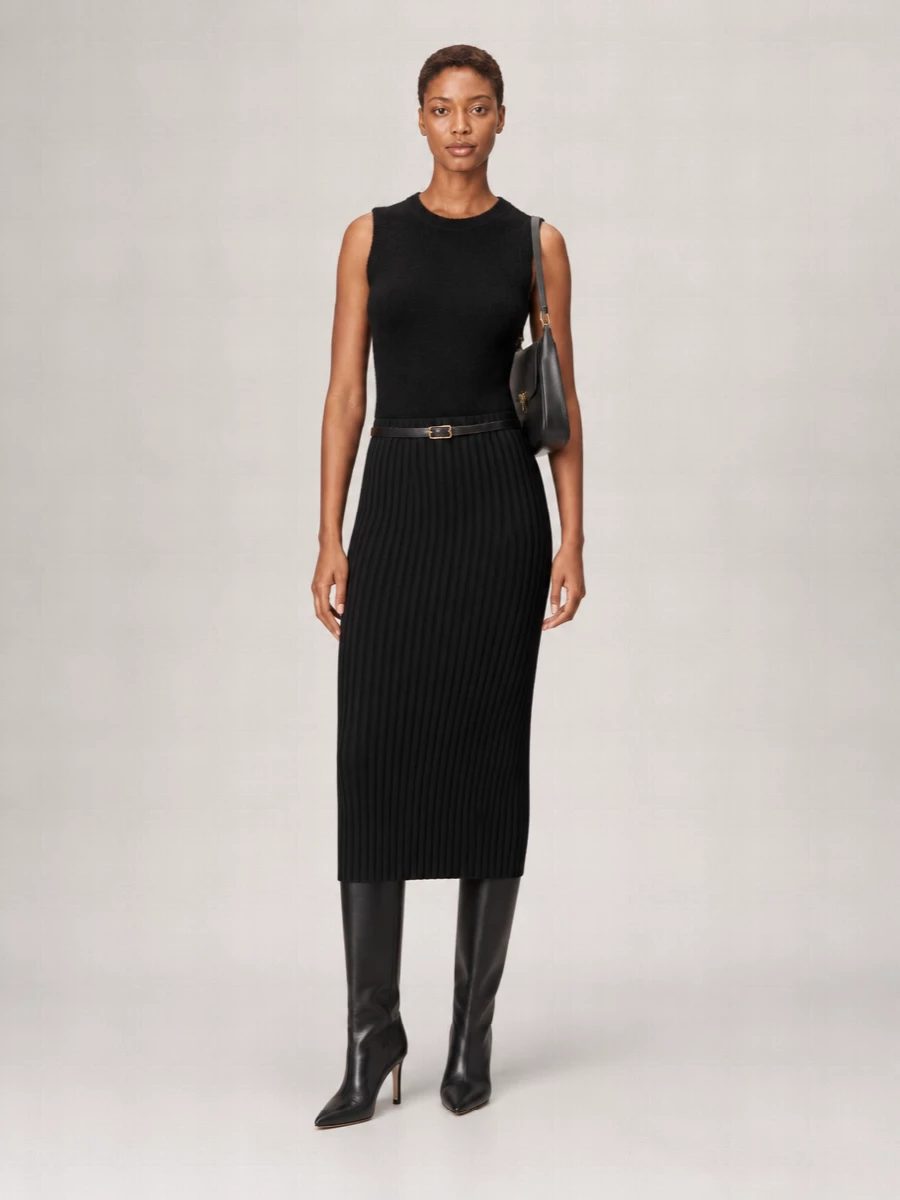 A black knit column from shoulder to hem keeps the silhouette clean, with the midi skirt and fuzzy tank reading as one continuous, tactile line. Pointed knee boots and a structured black shoulder bag sharpen the mood without breaking the monochrome. A slim leather belt quietly defines the waist, keeping the whole outfit in that restrained Italian quiet-luxury space, ready for office-to-dinner days year-round.