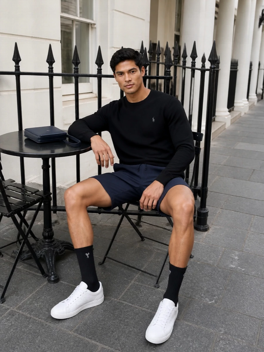 A black crew knit and navy deck shorts create a clean, East Coast preppy base that still feels grown‑up. White leather sneakers keep it sharp rather than sporty, while the refined navy crossbody and black socks add a subtle quiet‑luxury edge. Ideal for warm city days when you want relaxed ease with a precise, minimal palette.