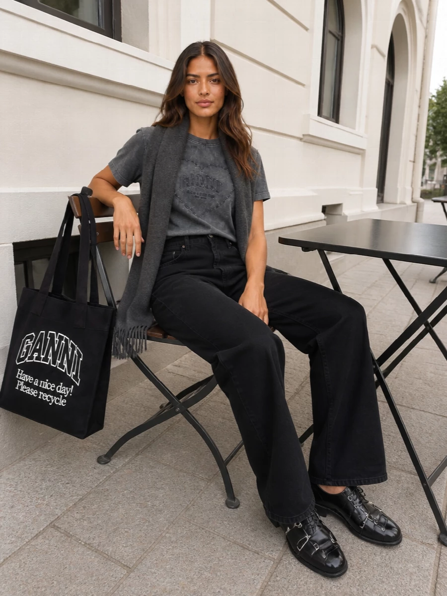 Washed charcoal on top and wide-leg black denim below create a slouchy, romantic-grunge base that feels considered but easy. Tough lace-up boots and a graphic logo tote lean into the streetwear mood, keeping the heart motif from feeling too sweet. A tonal charcoal scarf finishes the outfit with subtle texture and cold-weather practicality that still reads downtown.