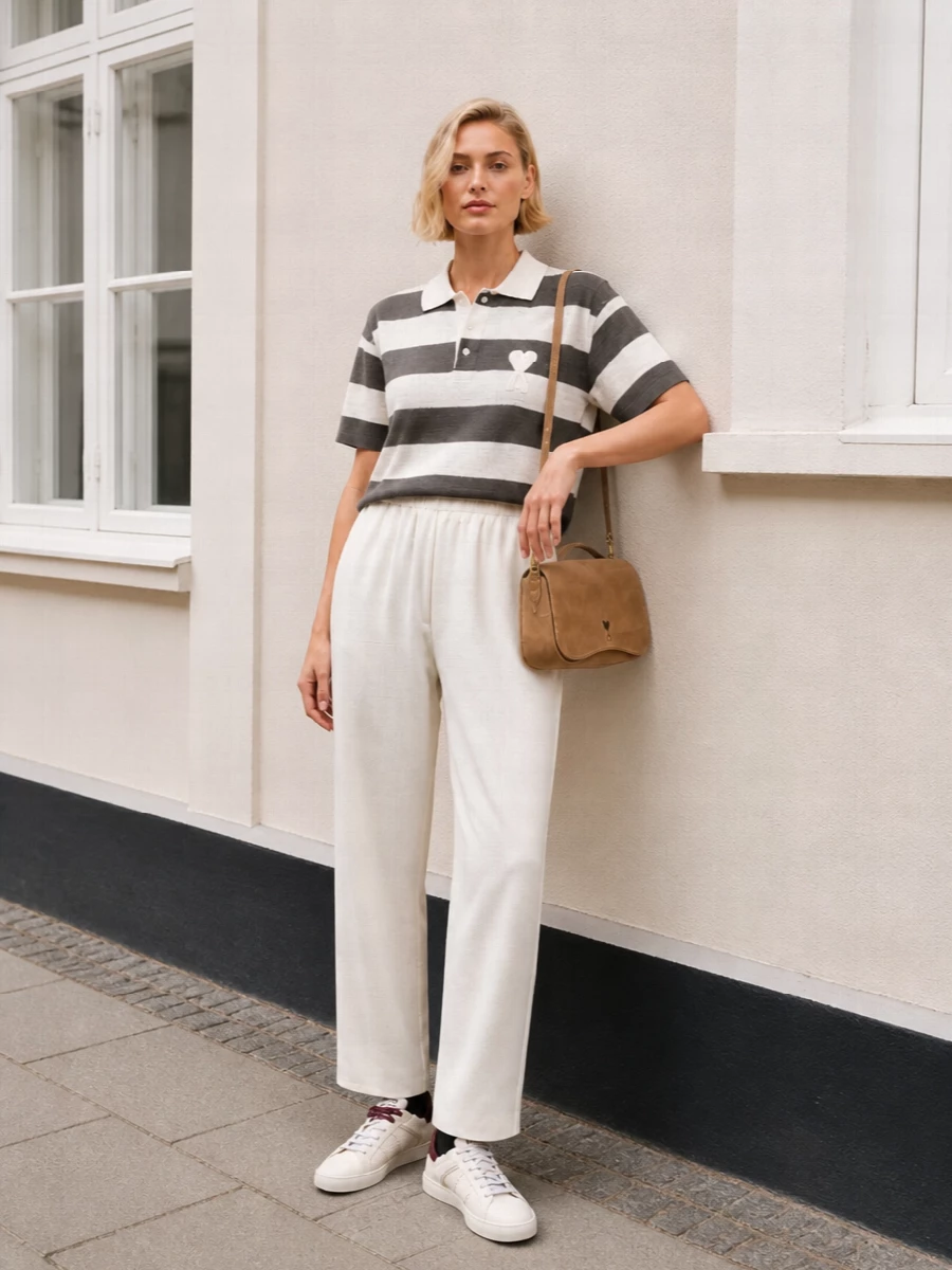 A striped Ami polo sits over high-waist off-white wide-leg trousers for a clean, relaxed take on city prep. Creamy canvas sneakers keep the mood easy, while a camel suede shoulder bag adds just enough warmth and structure. The palette stays soft and neutral so the bold stripes feel graphic but still low-key for daytime.