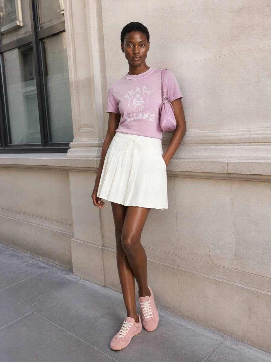 The dusky pink Prada logo tee is paired with the ivory pleated mini to create a fresh, collegiate-inspired SS look that feels light yet considered. Dusty-rose sneakers keep the palette soft and cohesive while grounding the outfit in relaxed sportiness, and the matching pink Givenchy shoulder bag adds just enough polish to take it from daytime errands to casual evening plans without losing ease.