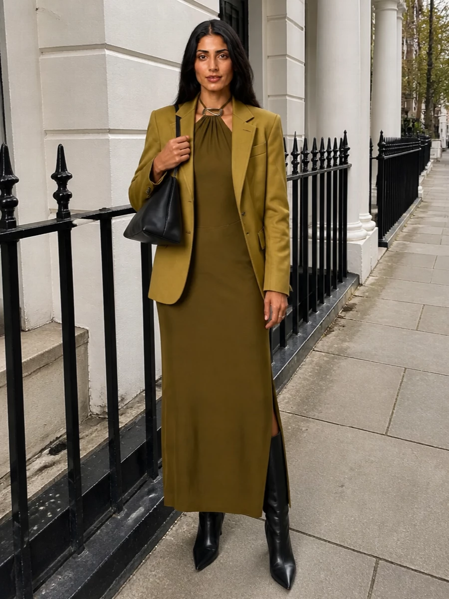 I am styling the Attico blazer over a single dress rather than tailoring separates so the mustard reads as a deliberate statement layer, not part of a competing suit story. The olive halter column, sharp black knee boots and sculpted black bag create a long, modern line that feels quietly powerful for evening, with the blazer adding warmth and structure without breaking the flow. The result is rich, tonal colour and clean, directional accessories that sit firmly in the same luxury universe as the jacket.