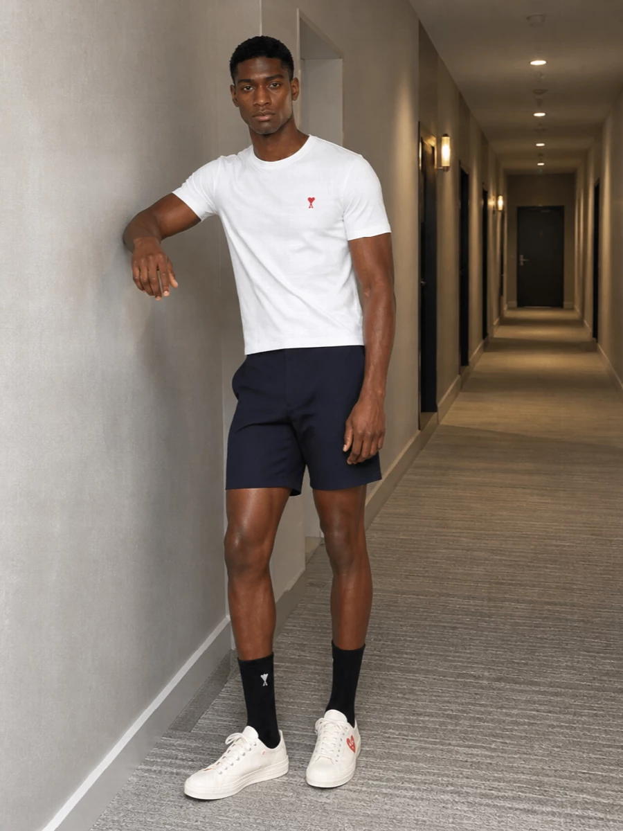 A crisp white Ami tee meets navy chino shorts for a clean, city-ready mix of street and preppy. Cream heart-detail sneakers pick up the tee’s red and white, while the bold striped tote finishes the palette with a graphic edge that still feels easy for everyday wear.