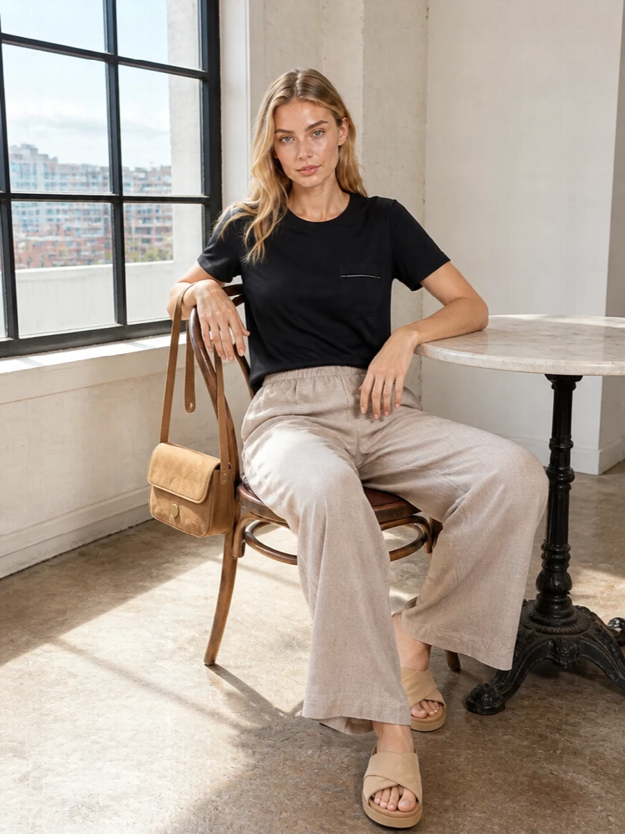 An inky black tee is softened with light taupe wide-leg trousers for a clean, summer-weight contrast that still reads calm and intentional. Sand suede slides and a compact camel shoulder bag keep the palette warm and tonal, while a blush-ivory scarf adds just enough light near the face for quiet polish from day to dinner.