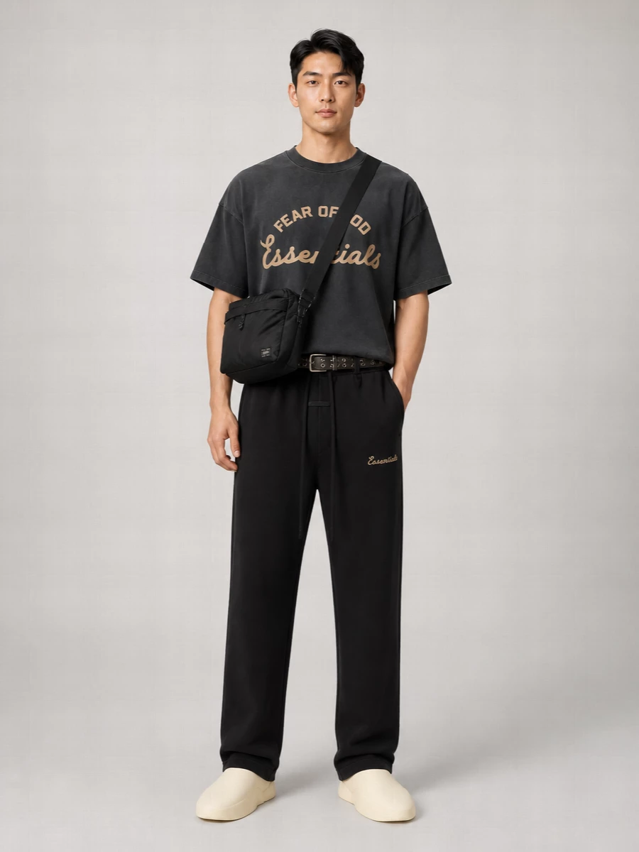 A head-to-toe Fear Of God Essentials base in black and washed charcoal keeps the mood calm and graphic, with the relaxed tee echoing the straight-leg pant’s easy attitude. Sculpted mules pick up the warm logo tones, while a low-key black messenger and grommeted belt bring just enough utility to feel city-ready without breaking the monochrome flow.