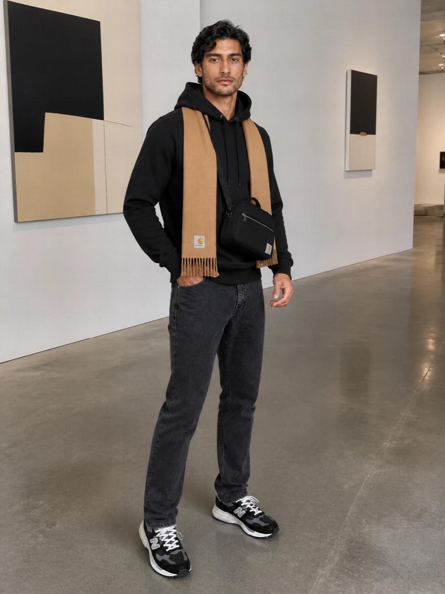 A weighty black hoodie sits over washed black denim for a clean, low-key street uniform that still feels considered. Black and charcoal runners keep the line relaxed and agile, while the compact crossbody and camel scarf add just enough utility and warmth without cluttering the silhouette.