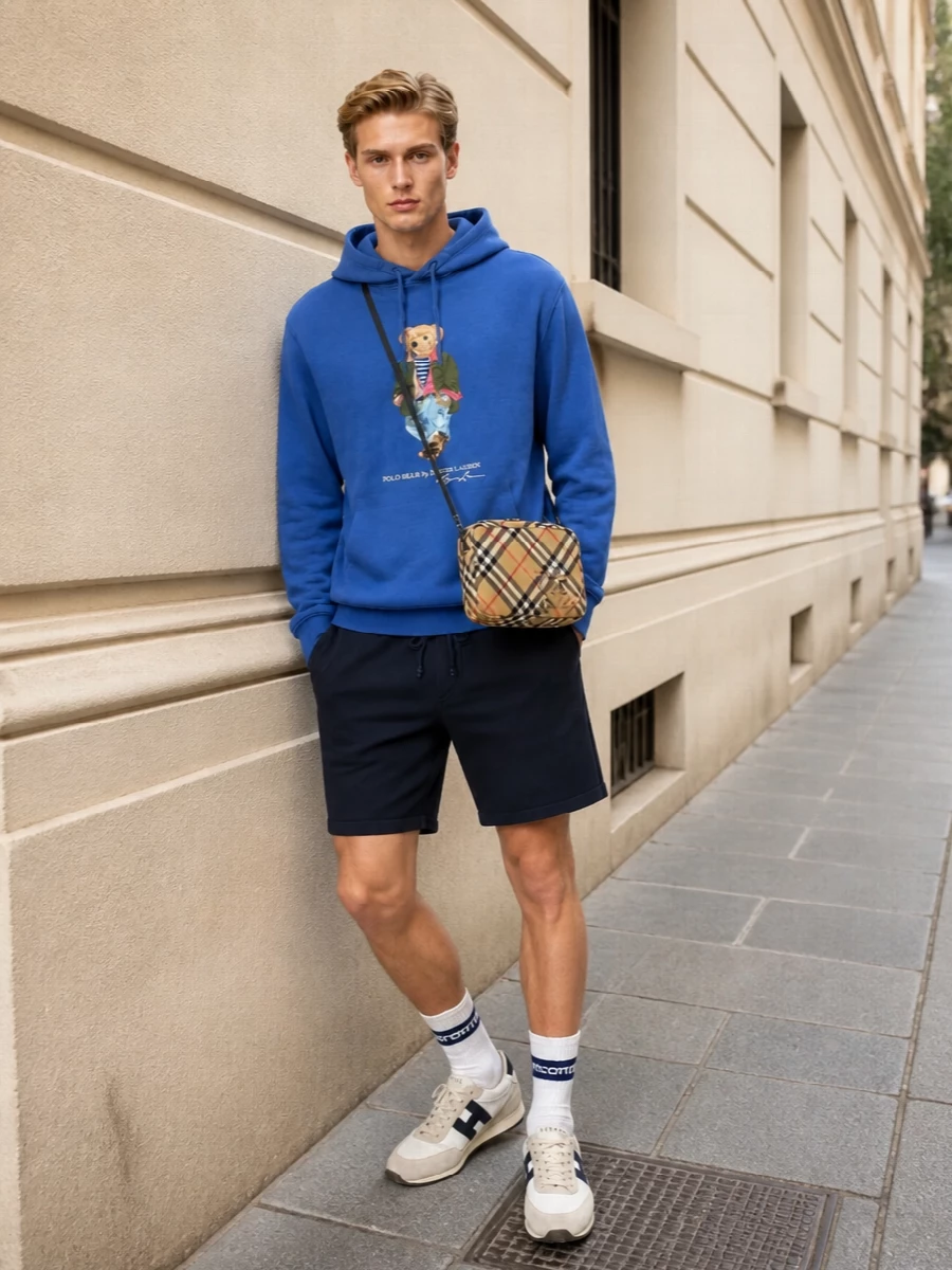 Cobalt, olive and navy come together with a relaxed campus energy, keeping the Polo Bear hoodie as the playful focal point. Clean navy shorts and sand-toned runners streamline the shape, while the checked crossbody and striped socks lean into polished, heritage sport rather than full streetwear. It feels easy for warm days but still considered enough for a coffee run or city wander.