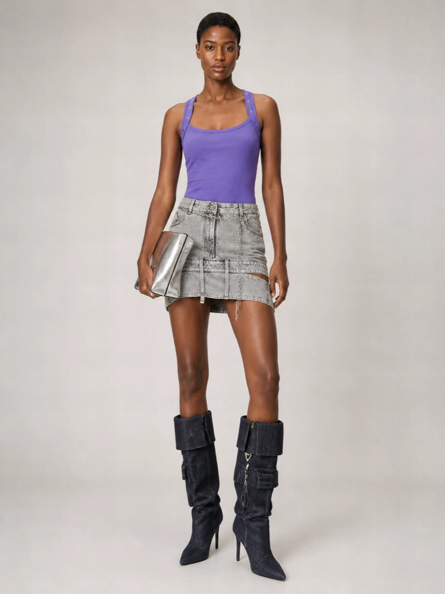 A saturated violet tank and reconstructed grey denim mini create a tight, high-rise silhouette that feels sharp, sexy and very night-focused. Inky denim knee boots extend the utility story and keep the palette controlled, while a silver chain belt and mirrored clutch add the right amount of flash without diluting the attitude. The result is pure Attico energy, built for late nights where the mini and hardware do all the talking.