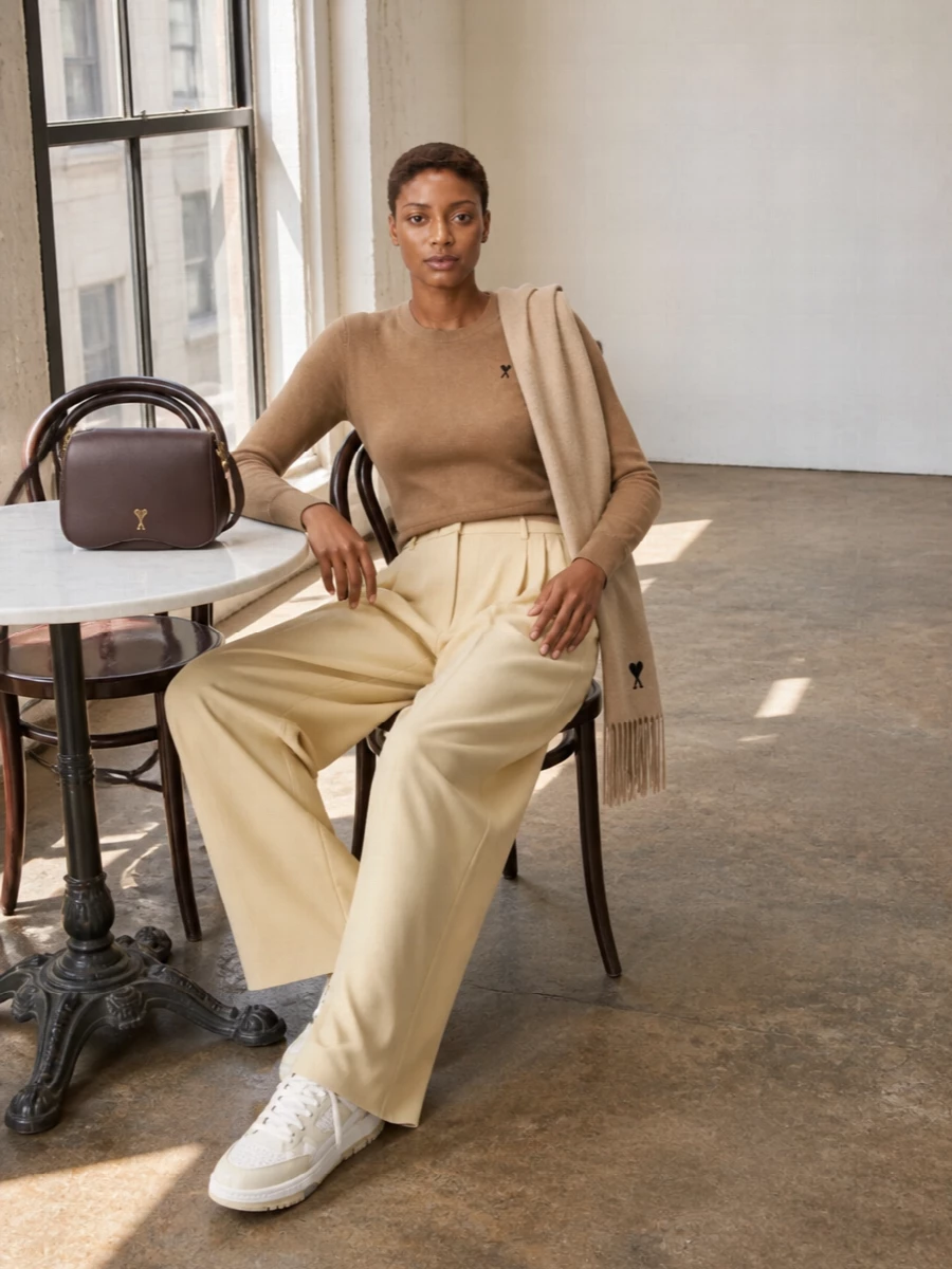 A cropped camel crew meets butter-toned wide-leg tailoring for a soft, elongated line that feels refined but easy. Neutral low-top sneakers keep the mood relaxed, while a structured chocolate shoulder bag grounds the palette with warm contrast. The camel scarf finishes the ensemble with subtle texture and a cohesive, tonal layer of warmth.