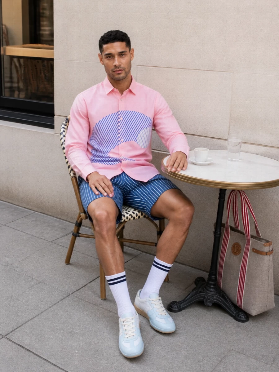 Soft pink shirting and navy striped shorts land in that sweet spot between gallery kid and coastal prep, with the shirt’s curved graphic playing against the linear stripe. Dip‑dyed sneakers and a striped canvas tote echo the palette without competing, keeping everything light and intentional for a sharp summer in the city. The result is relaxed, tailored and graphic, with the shirt firmly holding the stage.