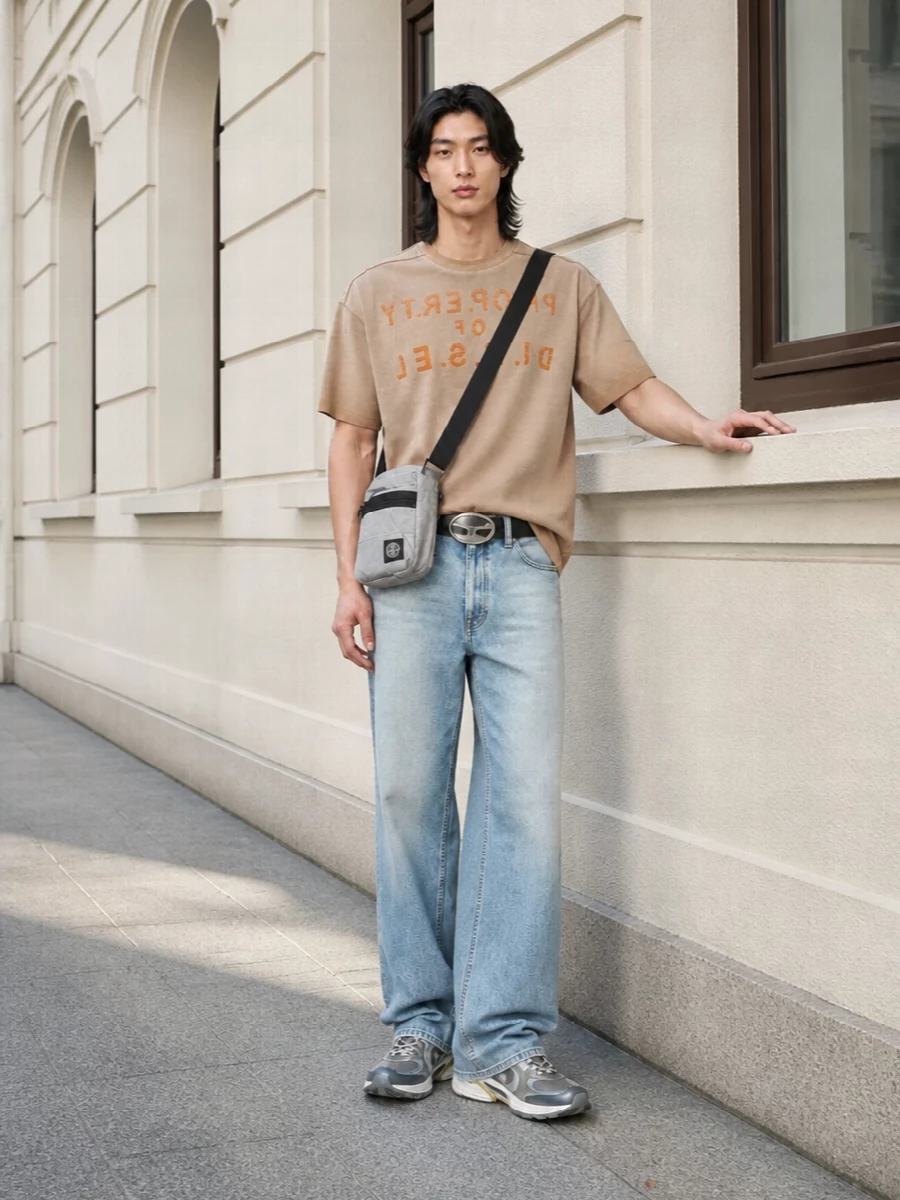 A sun‑faded Diesel tee sits over loose, washed light blue denim for a true early‑2000s street feel. Technical runners and a compact crossbody keep it city‑ready and fast, while the bold belt buckle quietly anchors the slouchy proportions. The palette stays soft and worn‑in, letting the graphics and textures do the talking.