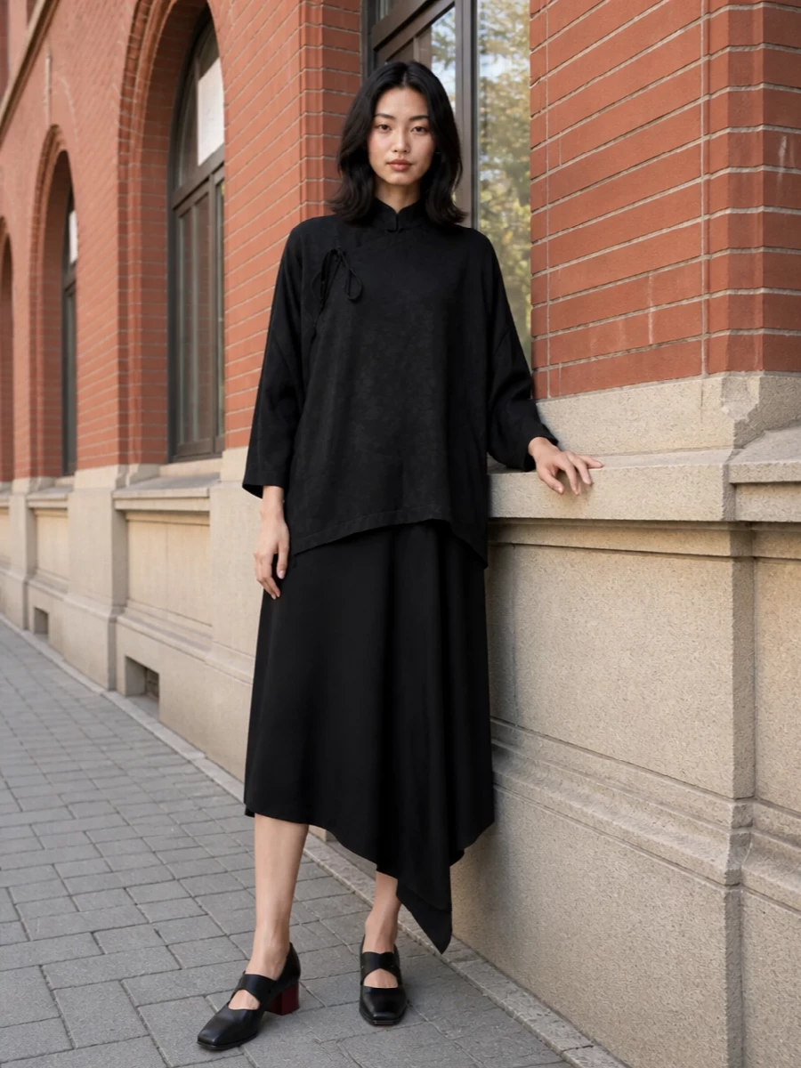I’m anchoring the Uma Wang tunic over the asymmetric black midi dress to create a long, inky column that feels ceremonial yet modern. The square-toe pumps with their oxblood heel and the sleek sculpted shoulder bag keep everything in the same quiet, architectural register, letting texture and drape do the talking. It is a gallery-dinner kind of ensemble, all shadowy layers and considered volume rather than overt shine.