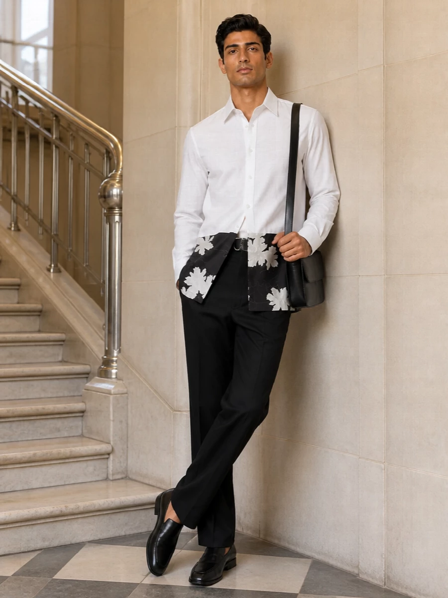 A long floral-hem shirt sits over clean black straight trousers for a precise, monochrome take on Dries’ romantic tailoring. Sleek black slip-ons and a minimal leather crossbody keep the line sharp, with a refined belt subtly defining the waist. The result is quietly dramatic city dressing, suited to gallery evenings and considered daytime meetings alike.