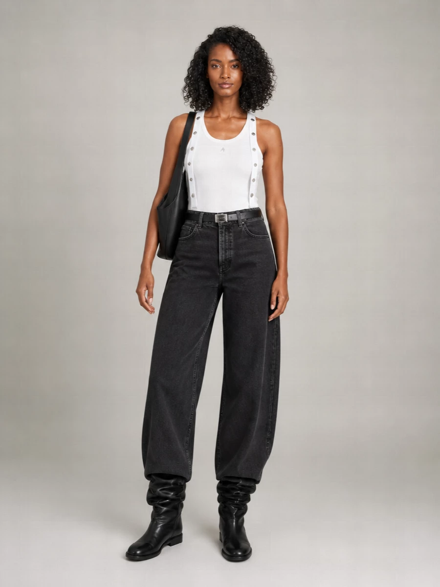Washed black wide-leg denim meets a longline white tank and sculptural flat boots for a clean, city-ready uniform with attitude. The high waist is quietly defined with a slim textured belt, while a curved black shoulder tote echoes the soft volume through the silhouette. The result is monochrome, directional and easy to wear day through late night with just a change of lip and jewelry.