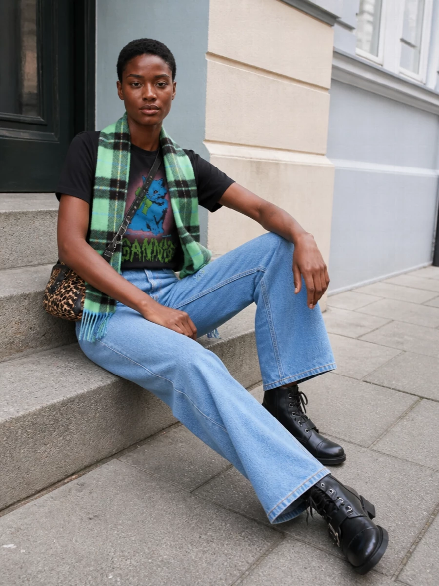 A washed-black graphic tee meets soft light-wash wide-leg denim for a relaxed, Copenhagen streetwear mood that still feels considered. Tough lace-up boots anchor the volume, while a compact leopard cross-body brings in just enough print and hardware to keep the outfit playful and night-out ready. The plaid scarf adds a hit of color and warmth without stealing focus from the cat graphic.