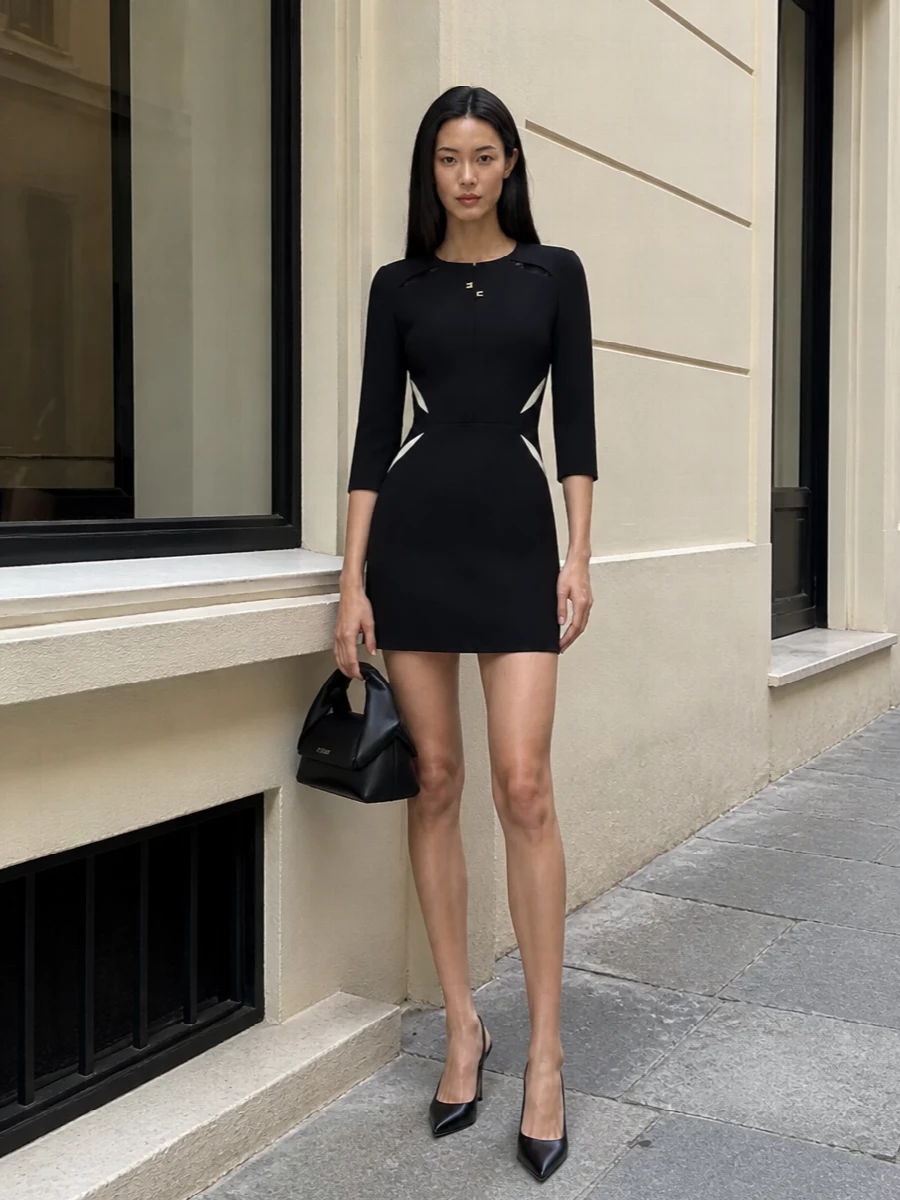 A sharply tailored Elisabetta Franchi mini is framed with equally precise accessories for a restrained, city-cocktail mood. The pointed Jimmy Choo slingback keeps the line elongated and graphic, while JW Anderson’s sculptural top-handle echoes the dress’s structure without distracting from the gold hardware. All-black with mixed metal subtly anchors the cream insets, so the cut and proportions stay center stage.