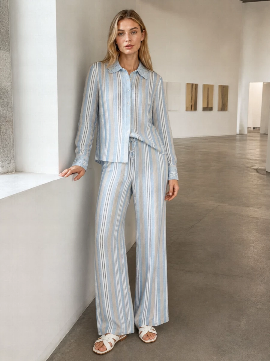 A Riviera-ready striped co-ord in powder blue and sand feels relaxed yet precise, with the longline shirt mirroring the fluid drape of the wide-leg trouser. White and tan woven slides keep everything light underfoot, while a structured raffia-and-leather top-handle and a whisper of sky-blue scarf bring just enough texture and color to feel considered, not busy.