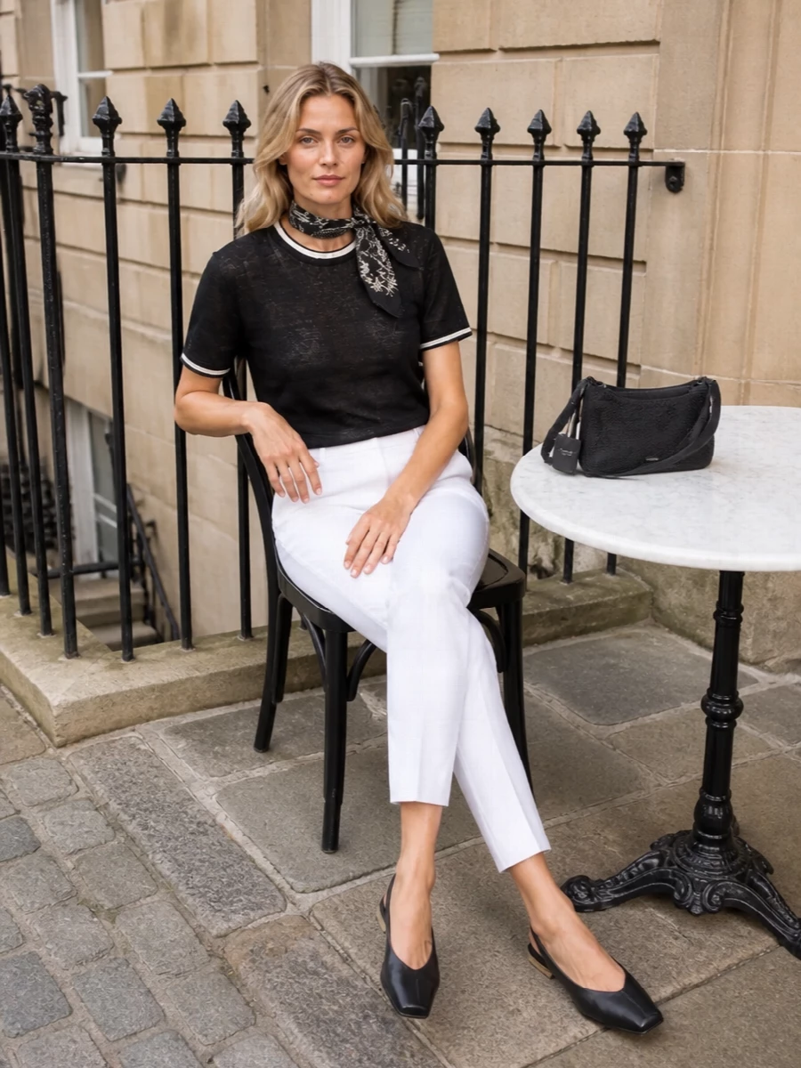 A sheer black knit tee is grounded with crisp soft-white tailoring for a modern, low-contrast monochrome ensemble. Square-toe slingback flats and a compact black baguette keep everything sharp yet relaxed, while a delicate printed scarf adds a whisper of softness without disturbing the clean lines.