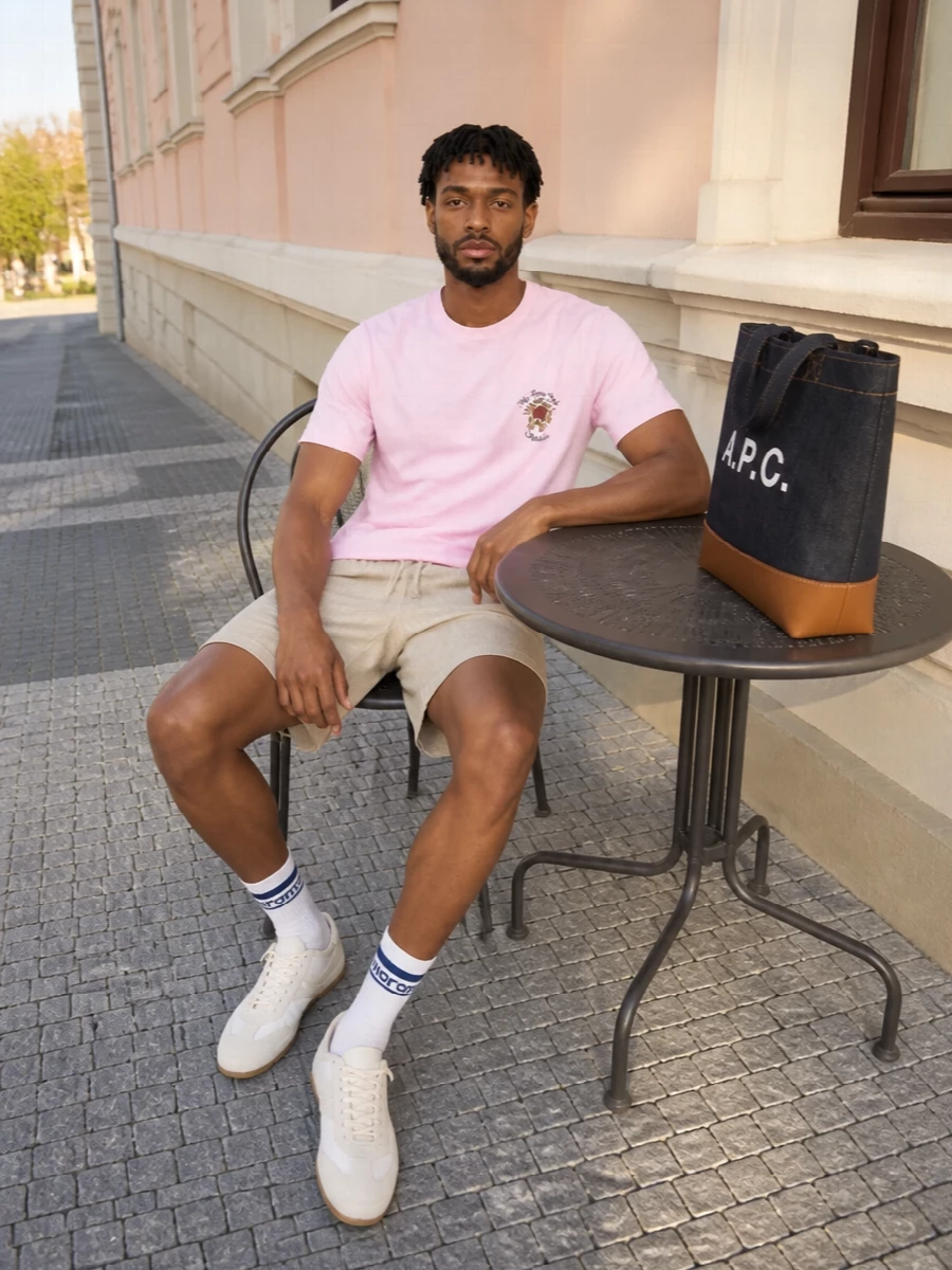 Soft pastel pink meets warm beige for a calm, romantic take on streetwear that still feels easy to throw on. The relaxed drawstring short and slim neutral runner keep the silhouette clean and unfussy, while the indigo tote and striped socks add just enough graphic contrast. It is an understated warm-weather outfit that feels considered without tipping into loud branding or heavy color.