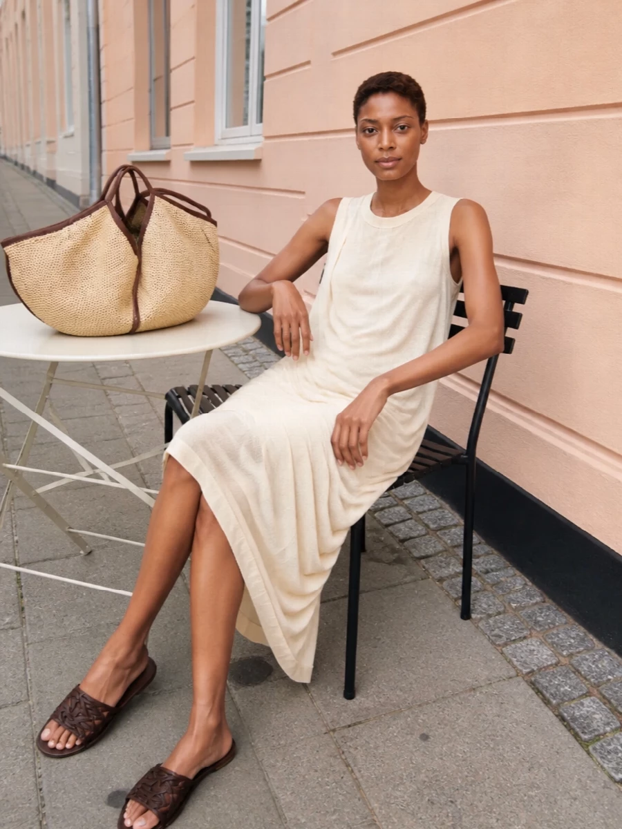 The buttercream asymmetric Rick Owens dress plays directly into the tote’s soft straw and brown story, keeping everything pale, fluid and quietly sculptural. I chose the dress route over separates here because one long, draped column feels more harmonious with the oversized tote’s organic shape than a broken-up top and trouser line. Dark brown woven slides tie back to the bag’s leather trim, giving just enough contrast and texture for a calm, sun‑ready outfit that moves from gallery afternoons to terrace dinners without trying too hard.