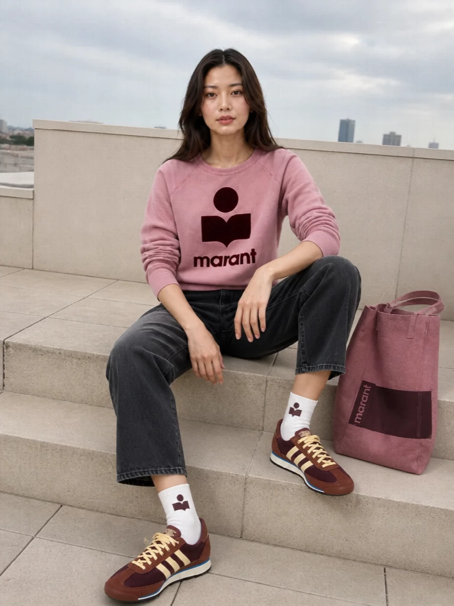 Dusty pink and deep burgundy stay in focus against washed charcoal denim, giving the sweatshirt a sharper, Paris-off-duty edge. Retro runners and a matching logo tote keep it relaxed and practical, while small logo socks add just enough detail at the ankle. The result is an easy spring city outfit that feels playful but grounded rather than sugary.