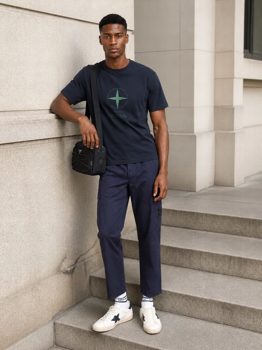 Navy on navy keeps this Stone Island pairing tight, with the straight-leg cargo grounding the slightly boxy graphic tee in clean street-sport energy. Off-white and navy Golden Goose sneakers break the block of blue just enough, while the Prada crossbody and striped socks nod to technical utility without crowding the silhouette. It is a calm, city-ready mix that feels premium but still easy to wear every day.
