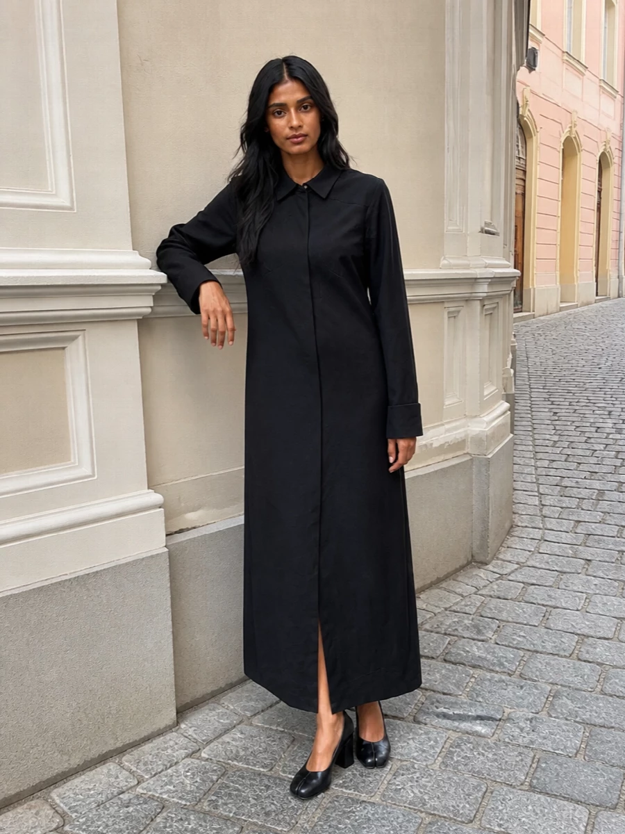This pairing leans into a pure black, tailored narrative, letting the structured tote and long shirt dress create one continuous, quietly commanding line. The sculptural block-heel pumps refine the proportion, adding discreet height without interrupting the minimalism. Choosing the dress path keeps the story very clean and focused, which aligns better with the bag’s restrained, boardroom-to-dinner attitude than breaking it up with separate tailoring pieces.
