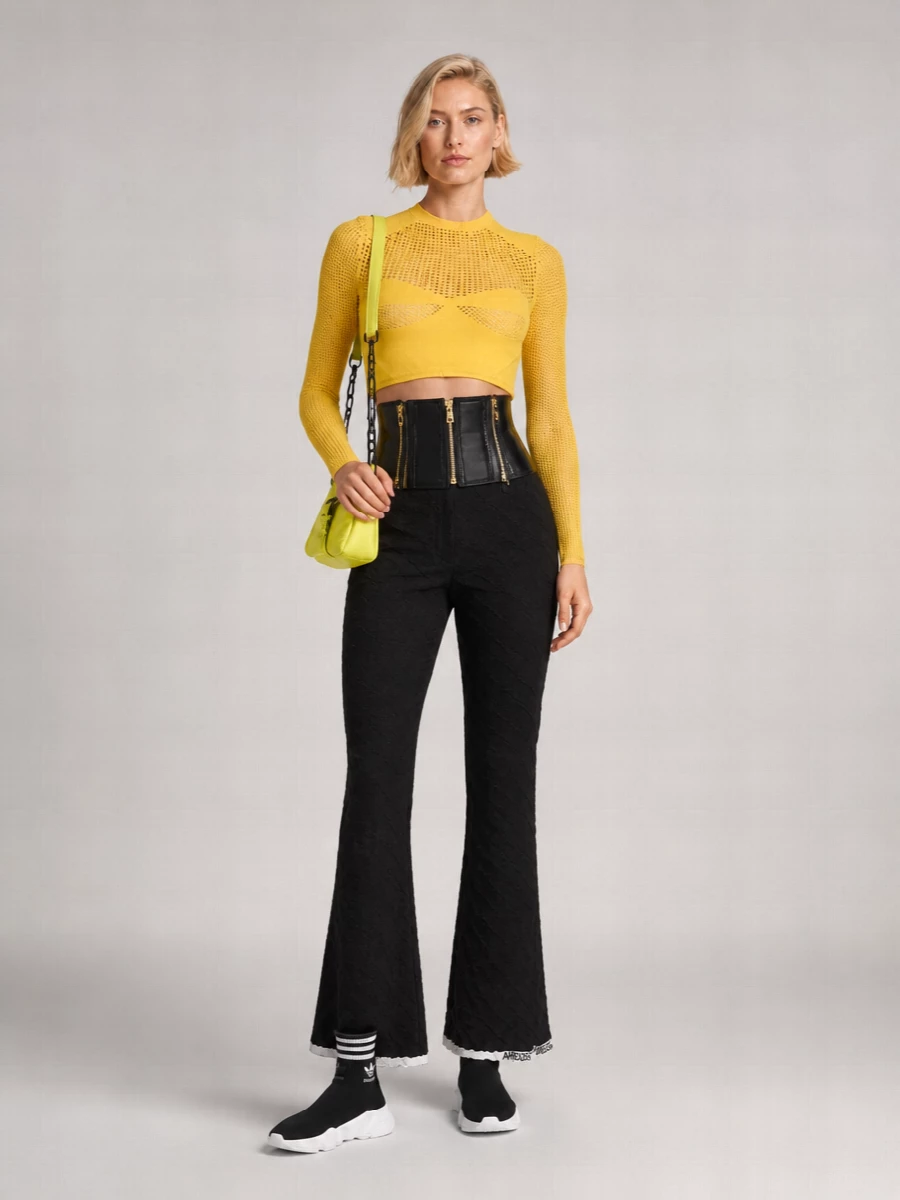 Ambush’s sheer yellow mesh top meets its match with sculpted black flares and a cinched corset belt, keeping the silhouette razor-sharp and nocturnal. Balenciaga sock sneakers ground the proportions in a clean, technical street register, while the neon mini bag repeats the yellow as a deliberate accent rather than an afterthought. The result is a high-impact city outfit that reads body-conscious, graphic and built for late hours under bright lights.