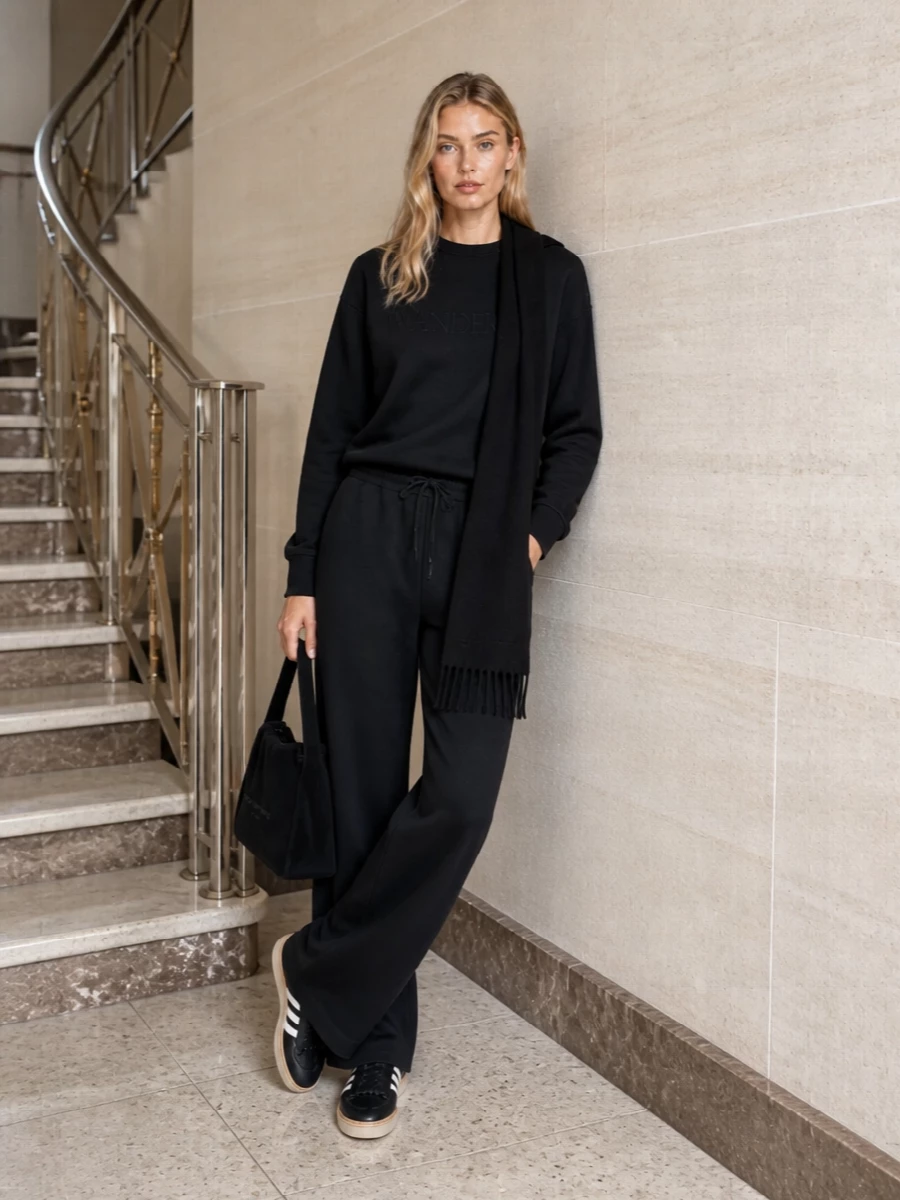 A head-to-toe black story keeps the JW Anderson sweatshirt firmly in quiet-luxury streetwear territory, balanced by the fluid volume of Y-3’s wide-leg track pants. Tonal sneakers and a soft Alexander Wang shoulder bag keep everything city practical while the long black scarf adds just enough texture and intention. The result is relaxed but sharply edited, ideal for travel days or off-duty time when you still want a considered silhouette.