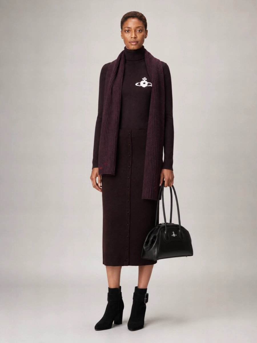 A deep eggplant turtleneck meets a slim espresso midi, keeping the line long, clean and quietly sensual. Black block-heel ankle boots and a structured top-handle sharpen it for city dinners or low-key office days. The plum scarf ties the darker tones together, adding just enough softness without breaking the minimalist mood.