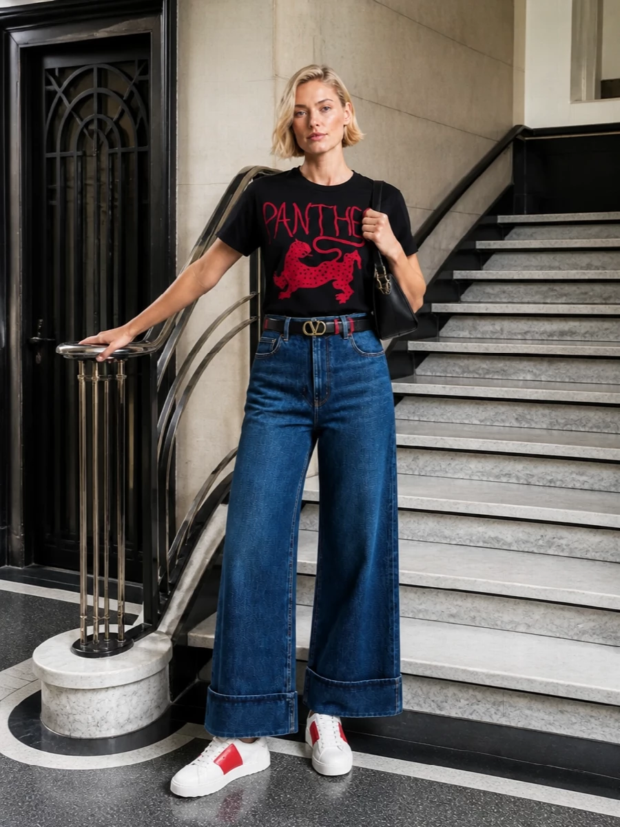 Valentino’s panther tee sits over sculpted wide-leg indigo denim for a graphic, quietly luxe take on streetwear. White and red sneakers pick up the feline print, while a black gold-chain shoulder bag and a slim logo belt keep the finish polished without diluting the attitude. The result is relaxed, confident and maison-signature from every angle.