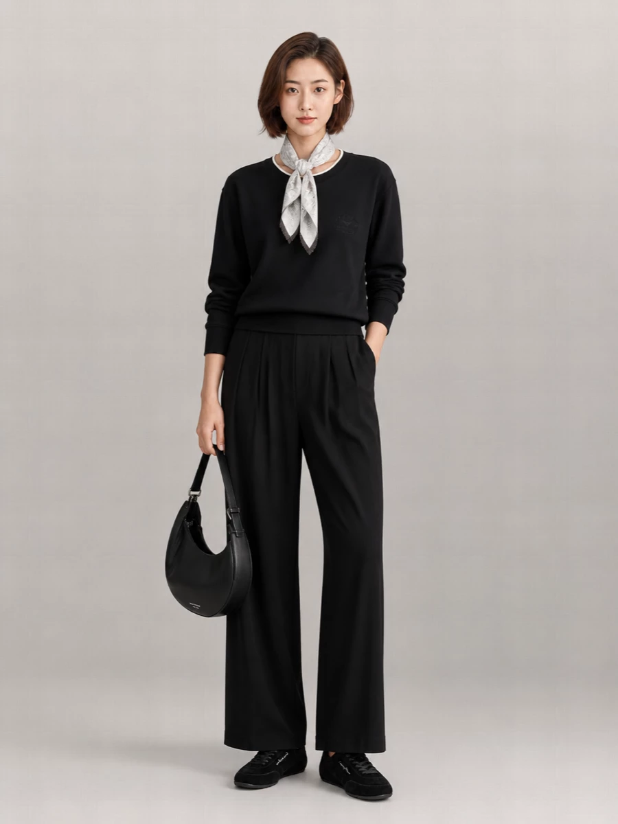A black-on-black base keeps this Emporio Armani set calm and grounded, with the relaxed sweatshirt and fluid wide-leg trouser reading sporty yet considered. The velvet sneaker and crescent bag add soft structure and texture without disturbing the minimal lines, while the pale scarf quietly lifts the neckline and picks up the contrast trim. It is an easy, monochrome off-duty uniform that still feels ready for a city day out.