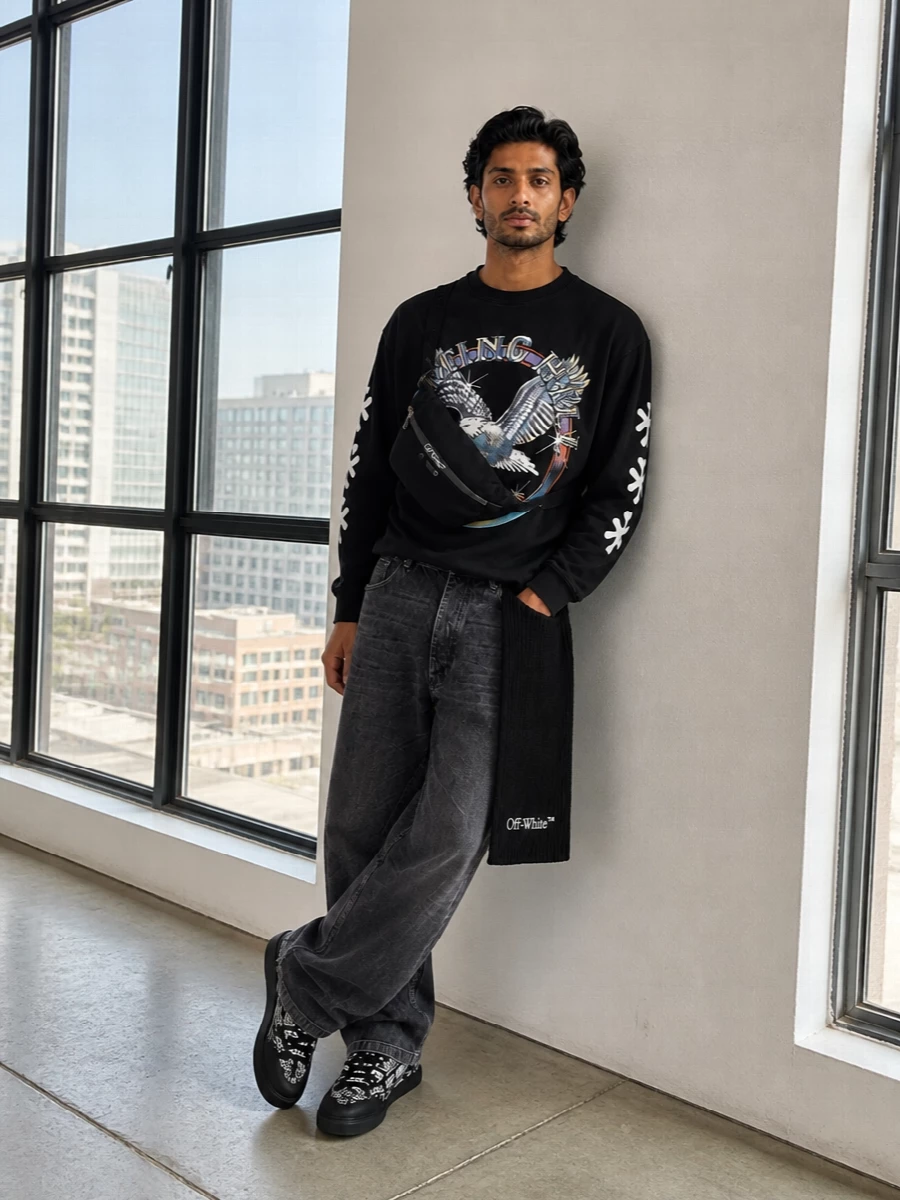 Tour-tee energy goes city-ready with washed charcoal denim that hangs loose but clean, keeping the eagle graphic in focus. Graphic black and white skate sneakers echo the print and keep the vibe relaxed, while the belt bag and scarf bring just enough logo detail to feel intentional without shouting. It is a cold-season streetwear uniform that feels lived-in, practical and clearly designer-level.