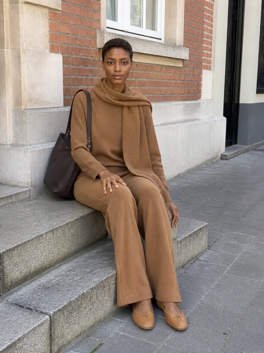 A tonal Max Mara knit pairing in camel keeps the mood soft and discreet, with wide-leg trousers that echo the sweatshirt’s ease yet read refined for the city. Camel Margiela ballerinas and a deep chocolate Max Mara bucket bag add a subtle play of textures and depth while staying within a restrained neutral palette. A matching camel scarf finishes the outfit with quiet warmth and continuity rather than contrast.