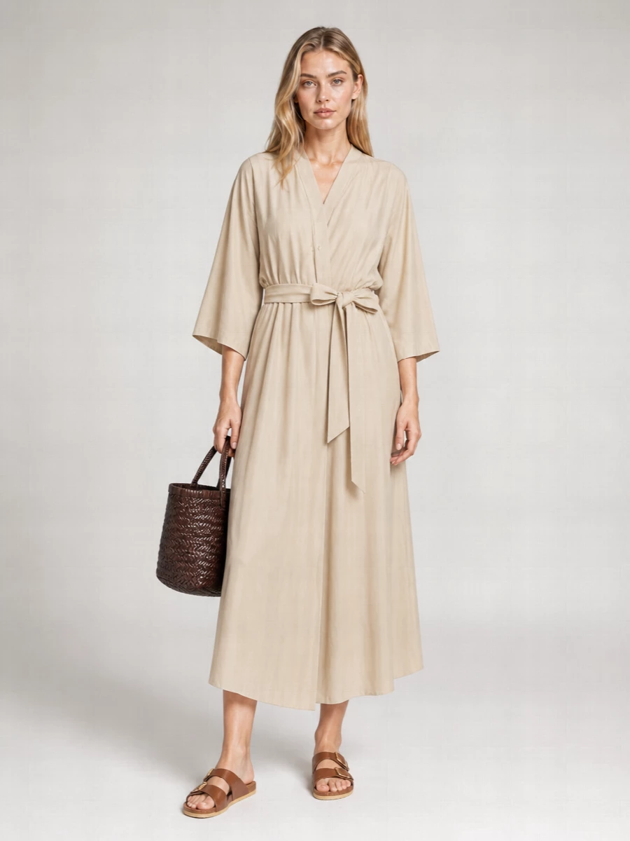 A sand-toned wrap dress and dark woven basket tote create a calm, sun-ready palette that feels modern yet relaxed. The self-tie waist softly defines the shape while keeping movement easy. Tan leather slides echo the bag’s warmth, pulling everything into a quiet, minimal summer outfit that works from market strolls to terrace lunches.