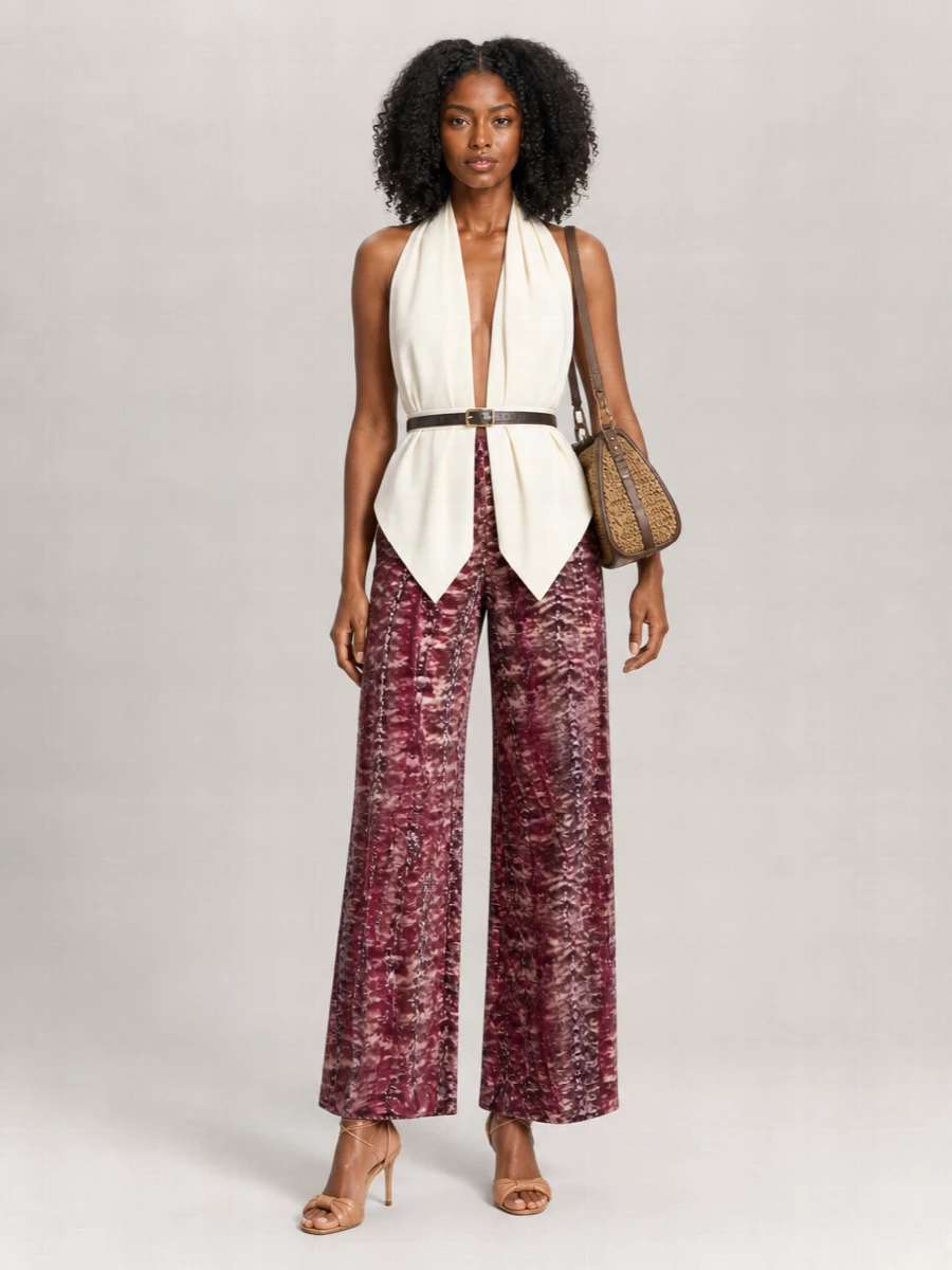 Alberta Ferretti’s tie-dye wide leg pant is grounded with a sculptural ivory halter, keeping the mood romantic yet sharply defined. Tan ankle-tie heels and a woven Etro shoulder bag pick up the trouser’s warmth, reading bohemian but decidedly refined. A slim black belt adds just enough structure at the waist to keep the flowy volume intentional rather than relaxed.