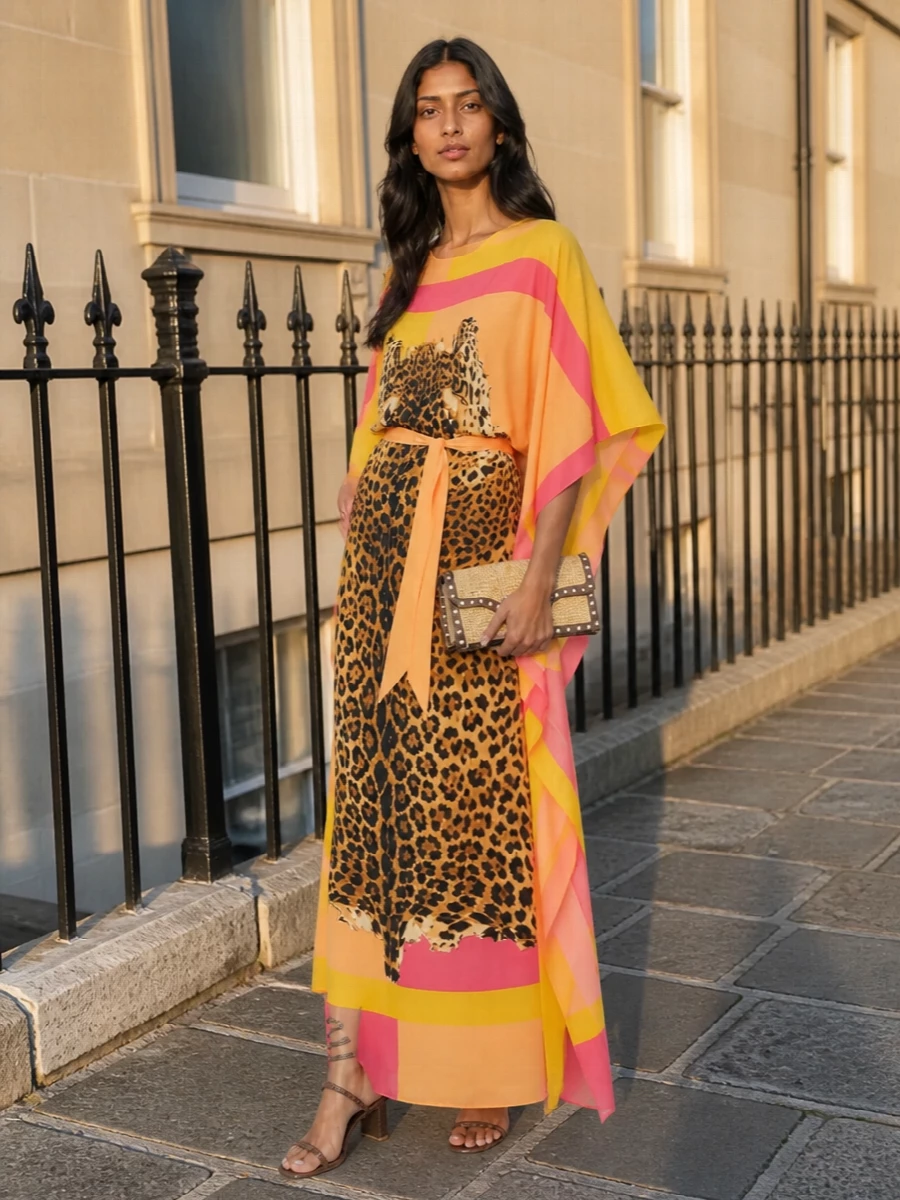 A Roberto Cavalli kaftan in sunlit peach and yellow takes center stage, its leopard motif framed by warm metallic accents. Chestnut crystal-wrapped sandals and a tan-trimmed raffia clutch keep the palette grounded in golden neutrals, letting the print do the talking. A silk scarf in soft corals is the final romantic touch, whether knotted at the waist or in the hair for long, luminous summer evenings.