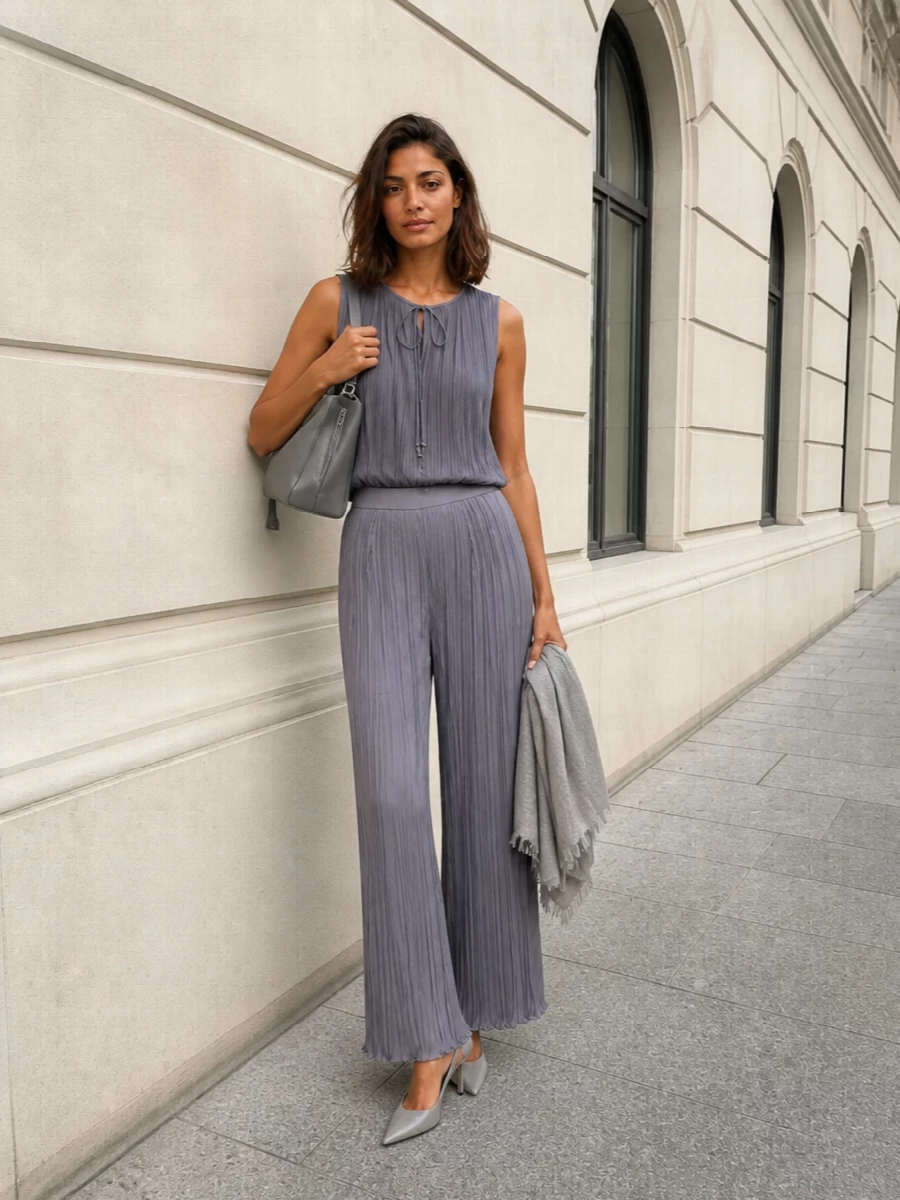 A slate and soft grey column feels calm yet decisive, with pleats catching the light in one continuous vertical line. Sharp grey slingbacks and a sculpted top-handle bag refine the softness into something dinner-ready and precise. The gauzy scarf is there only if you want a barely-there layer of texture around the neckline or shoulders.