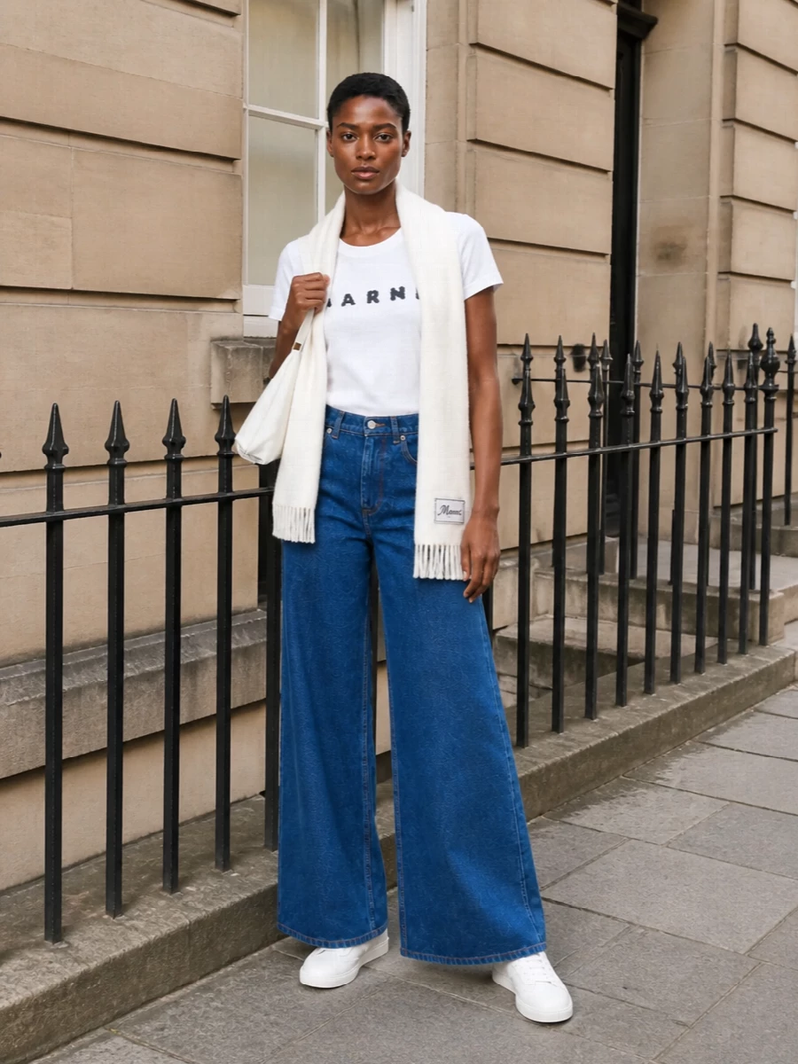 A crisp Marni tee meets high-rise wide-leg indigo denim for that art-student-in-the-city uniform, all clean lines and easy attitude. White leather sneakers keep the foundation sharp but unfussy, while the sculptural white shoulder bag and ivory scarf add just enough structure and softness to feel considered without trying too hard.