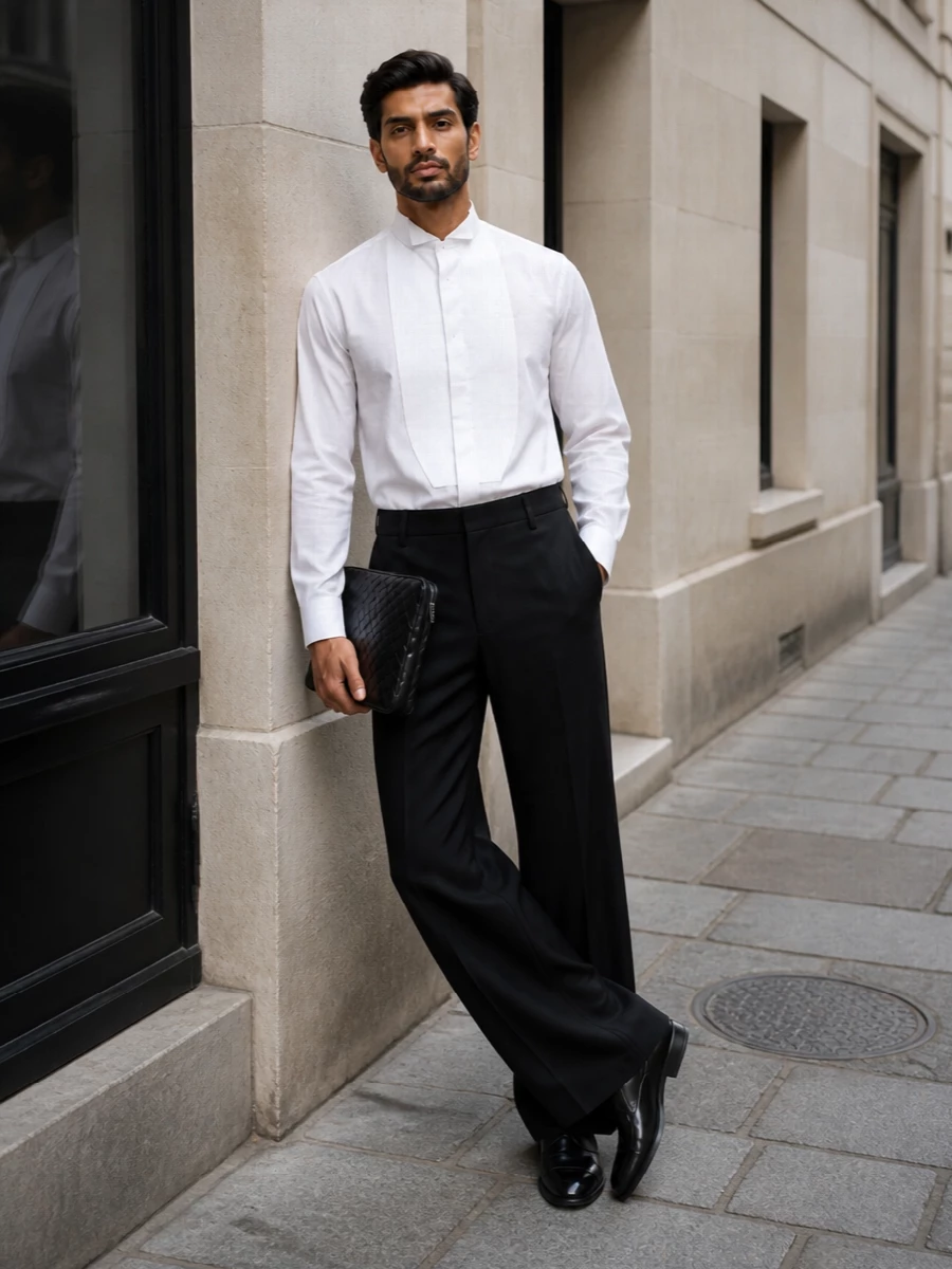 This look is a modern, minimalist take on black tie: the crisp white wingtip tuxedo shirt is grounded by fluid, wide-leg black trousers and anchored by the perforated Gucci oxfords. The proportions are relaxed but disciplined, and the black intrecciato clutch adds a final, textural note of quiet luxury without disturbing the clean monochrome palette.
