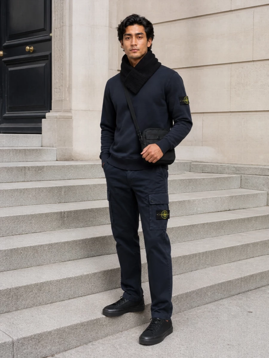 Deep navy and black keep this Stone Island set tight and streamlined, with the cargo trouser giving a more intentional, city-ready edge than pure sweats. The terrace-inflected black sneakers and compact crossbody stay within the same technical language, so the whole outfit reads calm, functional and quietly assertive. A sharp black scarf finishes the mix with warmth and structure without disturbing the minimalist street palette.